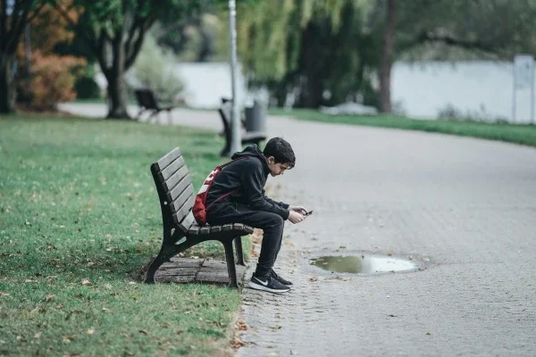 Teen boy sitting on a park bench looking at phone