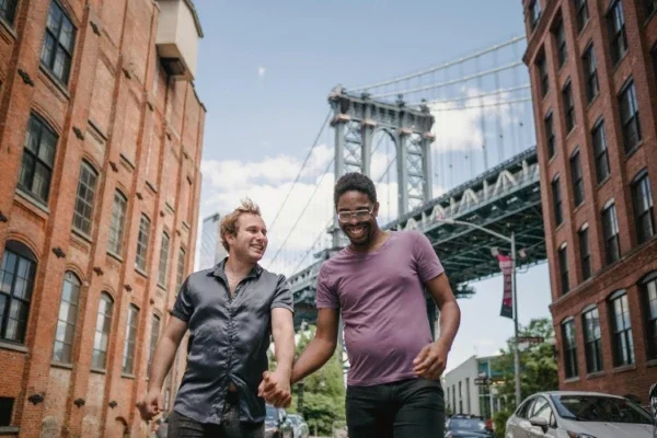 Two men holding hands in front of the Manhattan Bridge
