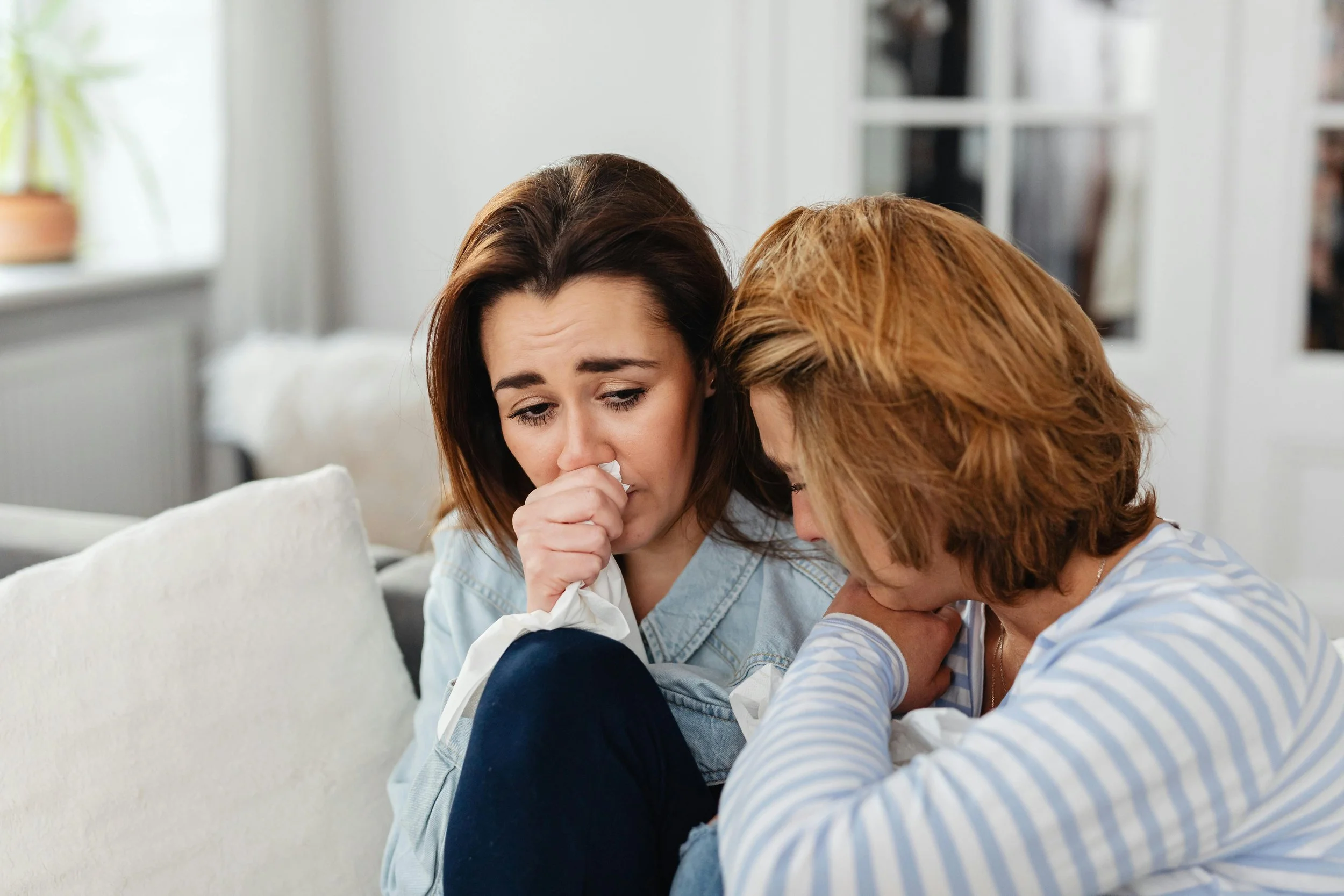 Two women sitting on a couch crying