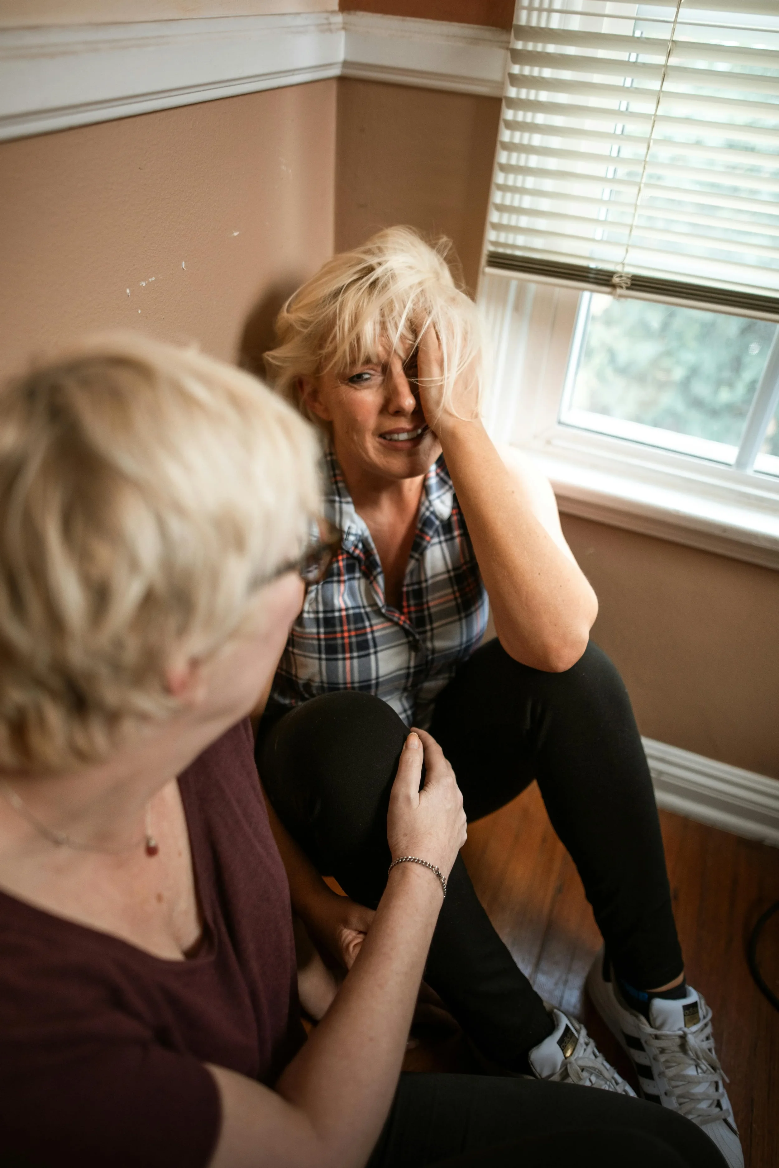 A woman comforting another woman sitting in the corner of a room