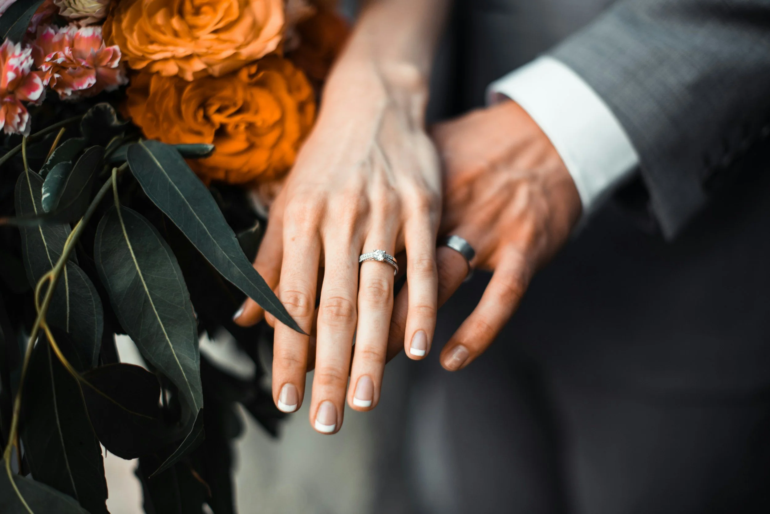 Close-up of a newlywed couple holding hands near wedding flowers, showing wedding rings on their fingers.