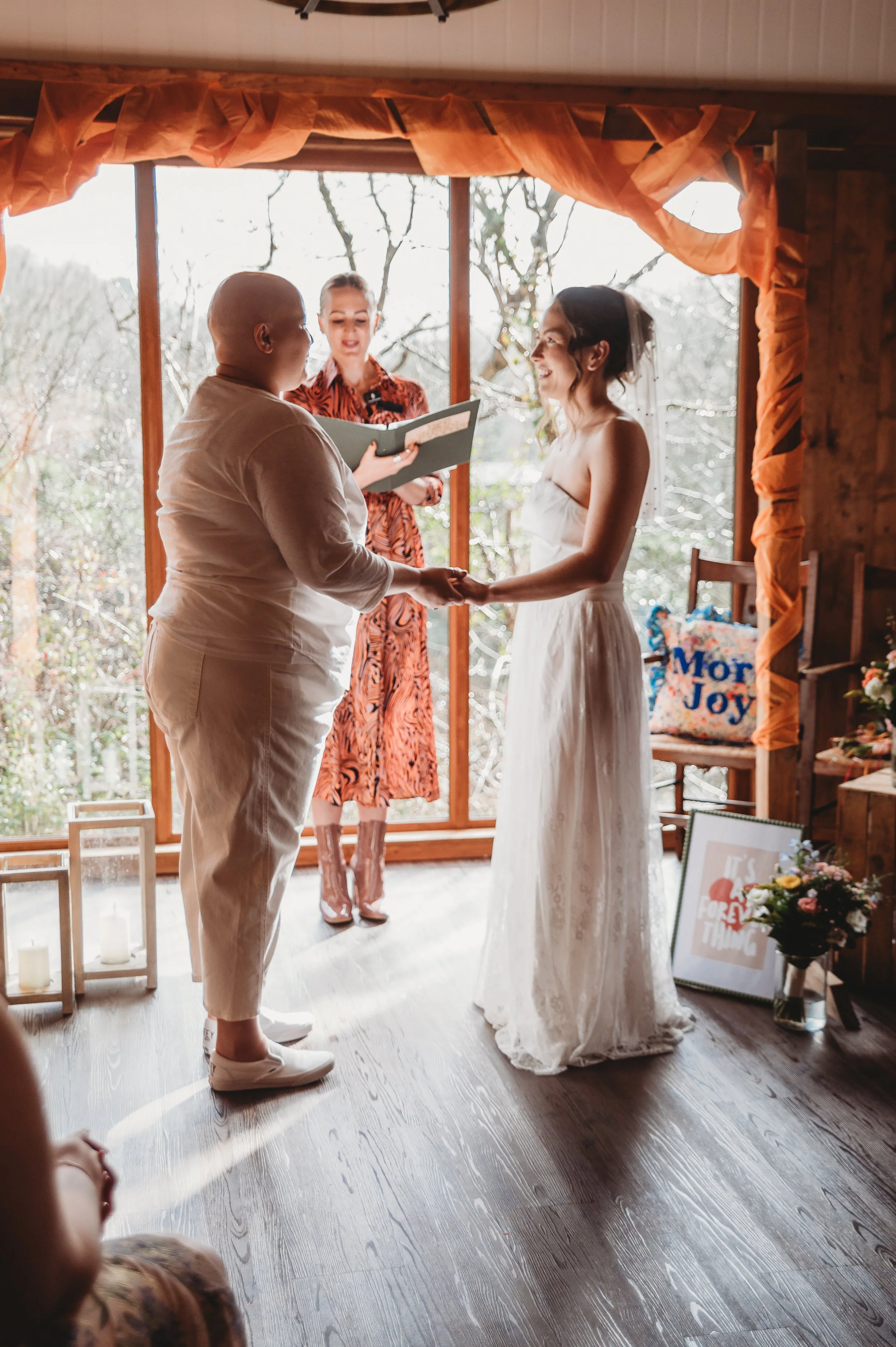 Close-up of a couple's hands showing wedding rings, with a bouquet of colorful flowers and green leaves in the background.