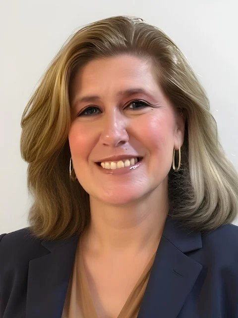 A woman with shoulder-length blonde hair, wearing hoop earrings and a dark blazer, smiling at the camera.