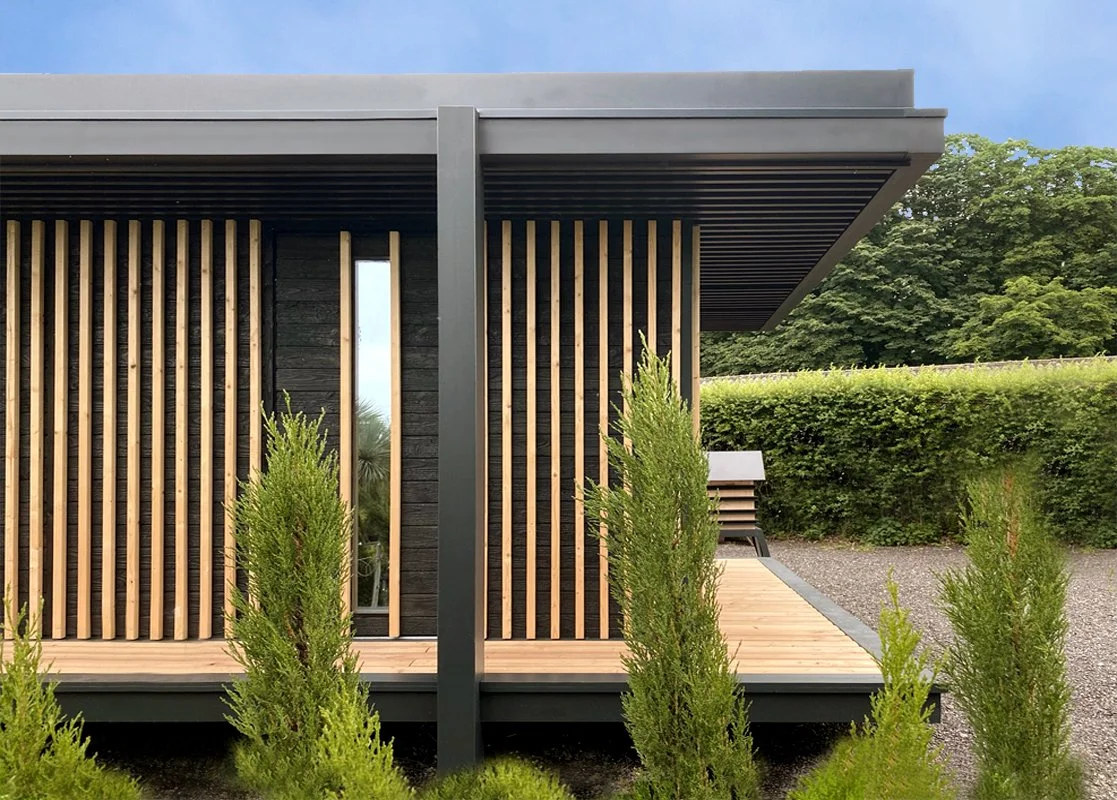 Une façade extérieure moderne d'un Ecolodge MEGYMA  avec des volets en bois vertical, un porche en bois et un petit jardin avec des arbustes verts.