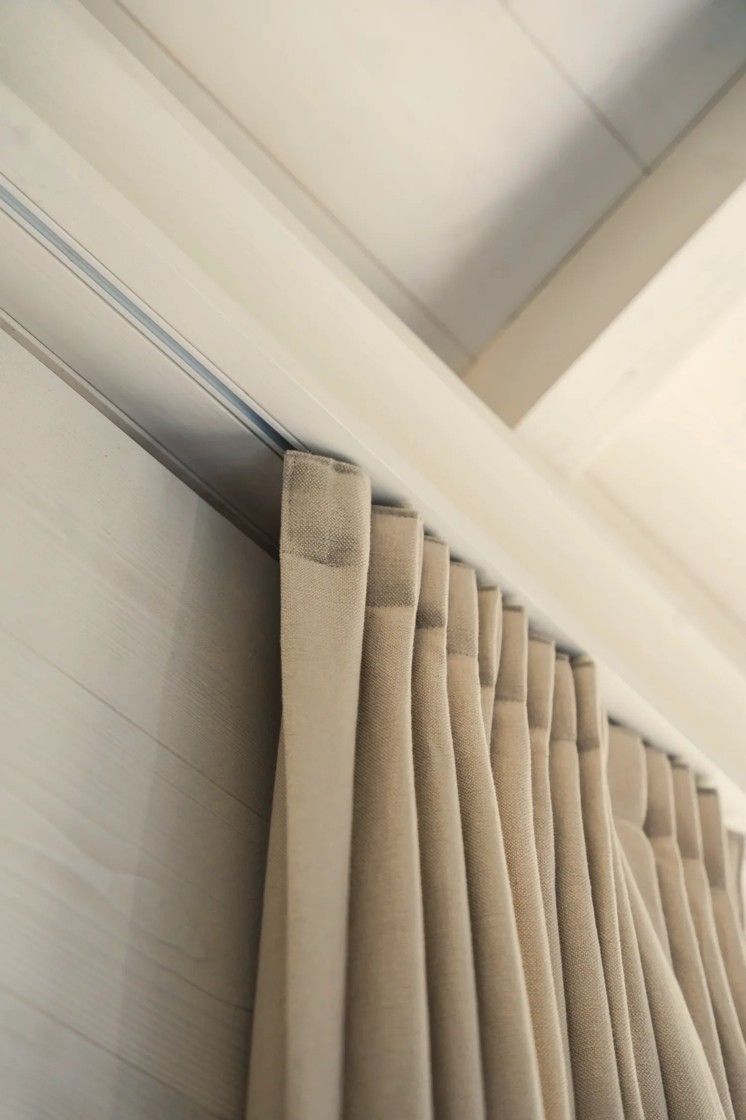 Rideau beige suspendu à une tringle métallique, avec des plis réguliers, dans une pièce éclairée.