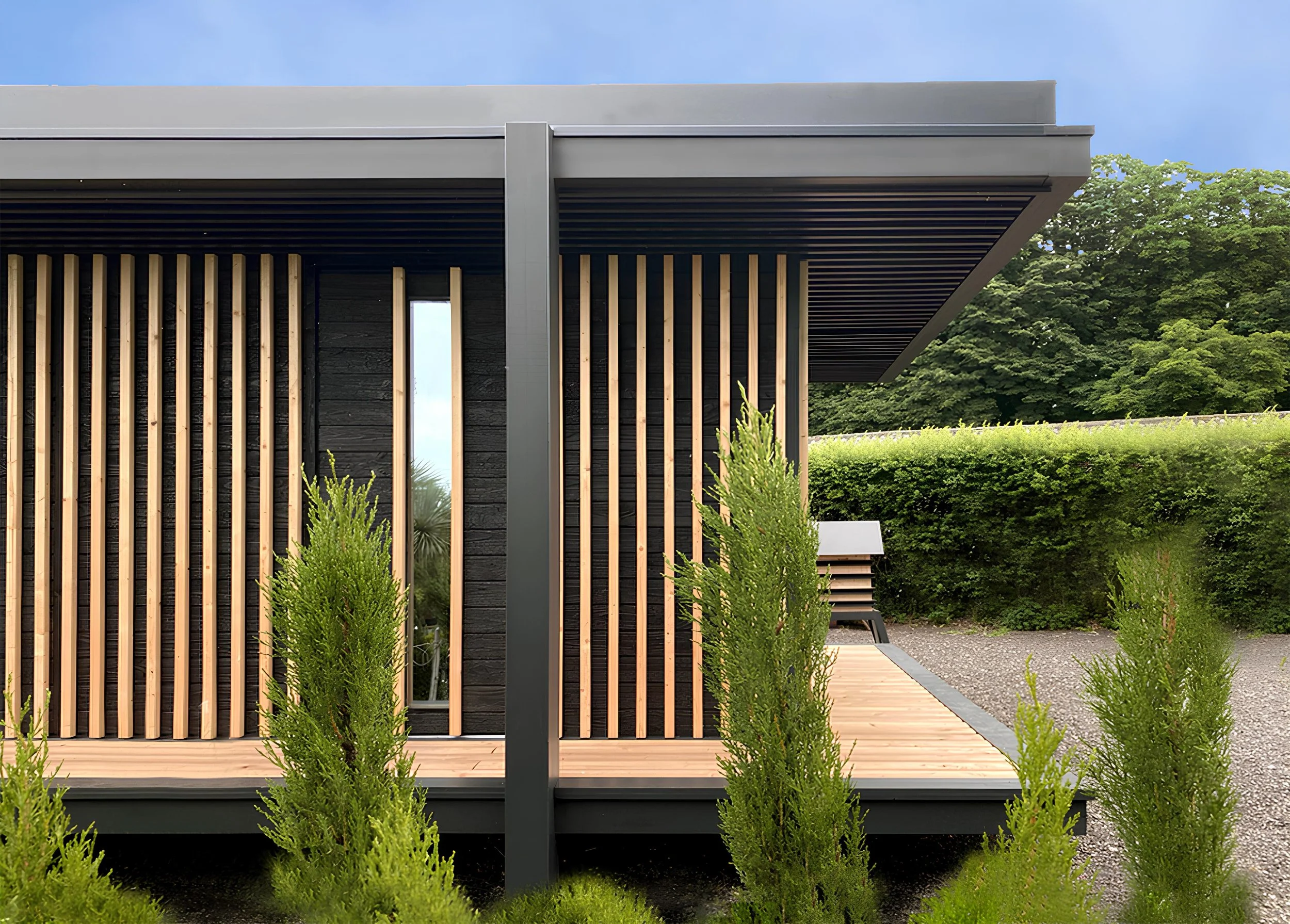 Vue d'un Ecolodge MEGYMA noir avec panneaux en bois vertical, fenêtres longues et étroites, entoure de verdure et d'un chemin en bois.