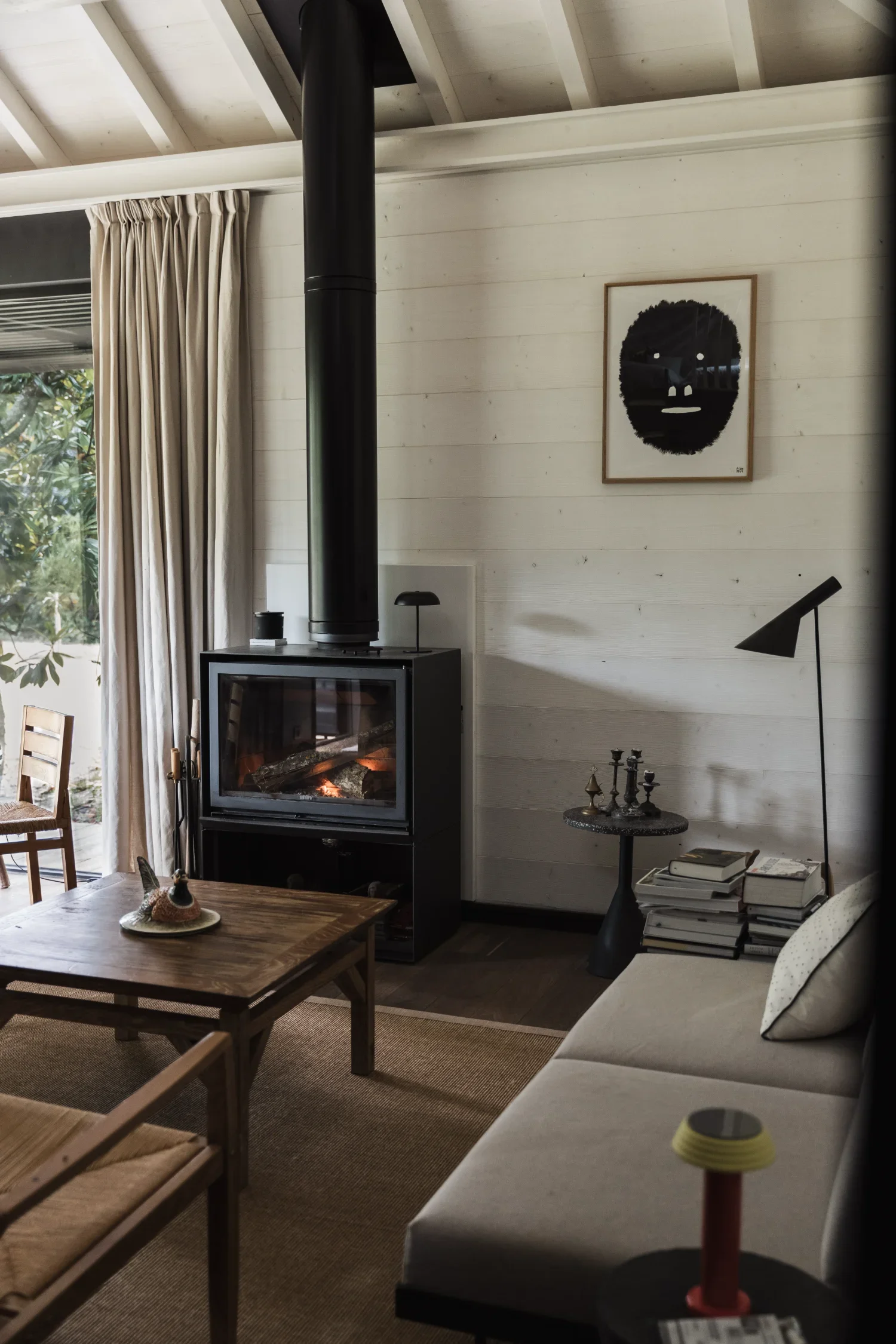 Intérieur d'un salon moderne avec cheminée, table en bois, canapé beige, étagère avec des livres, et décoration minimaliste.