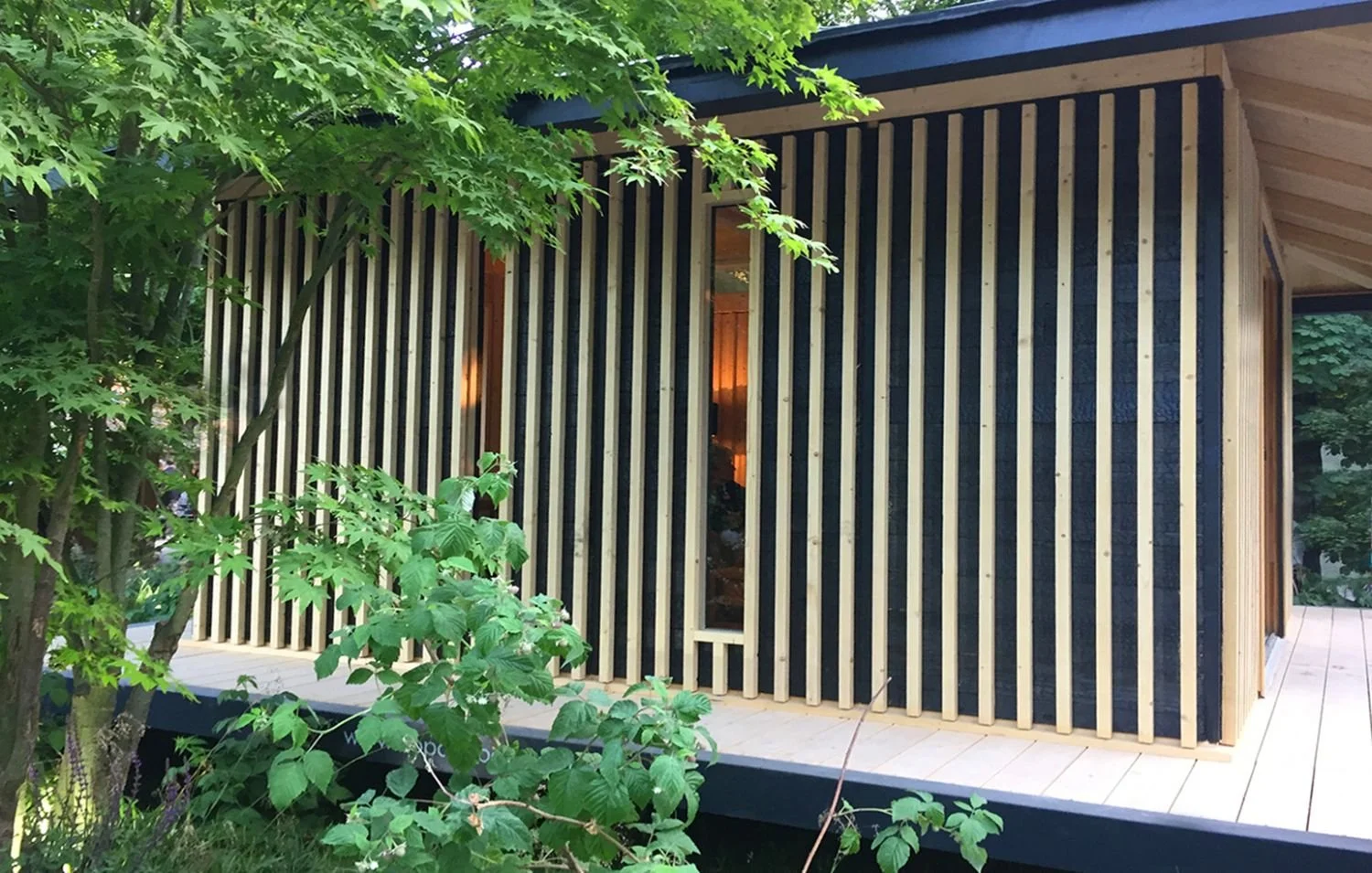 Façade d'un Ecolodge KOBE avec des murs en bois noir et des poutres en bois clair, entourée d'arbres et de végétation