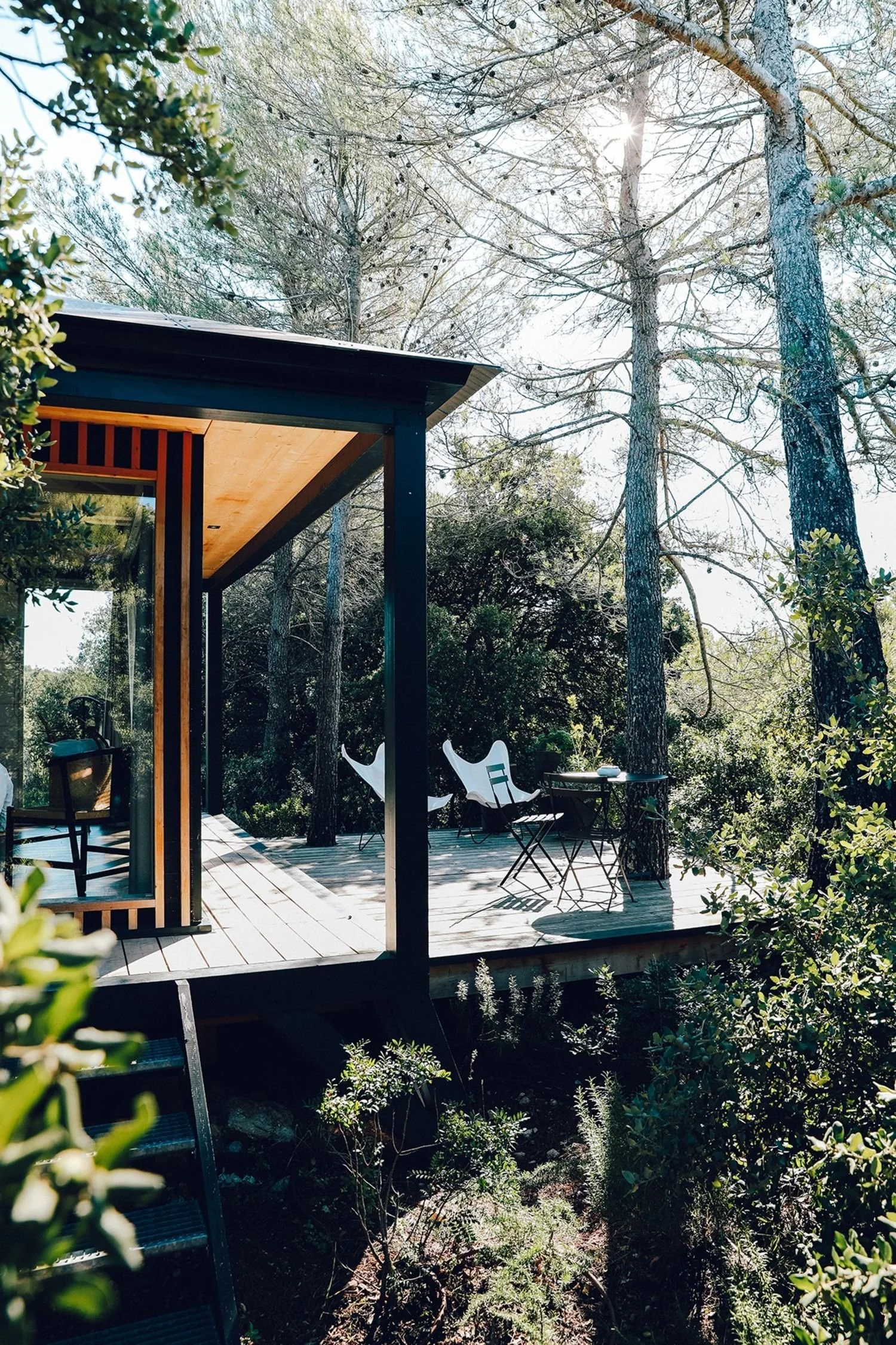 Ecolodge KOBE entourée d'arbres avec des chaises blanches et noires, une table, et une ambiance en plein air ensoleillée.