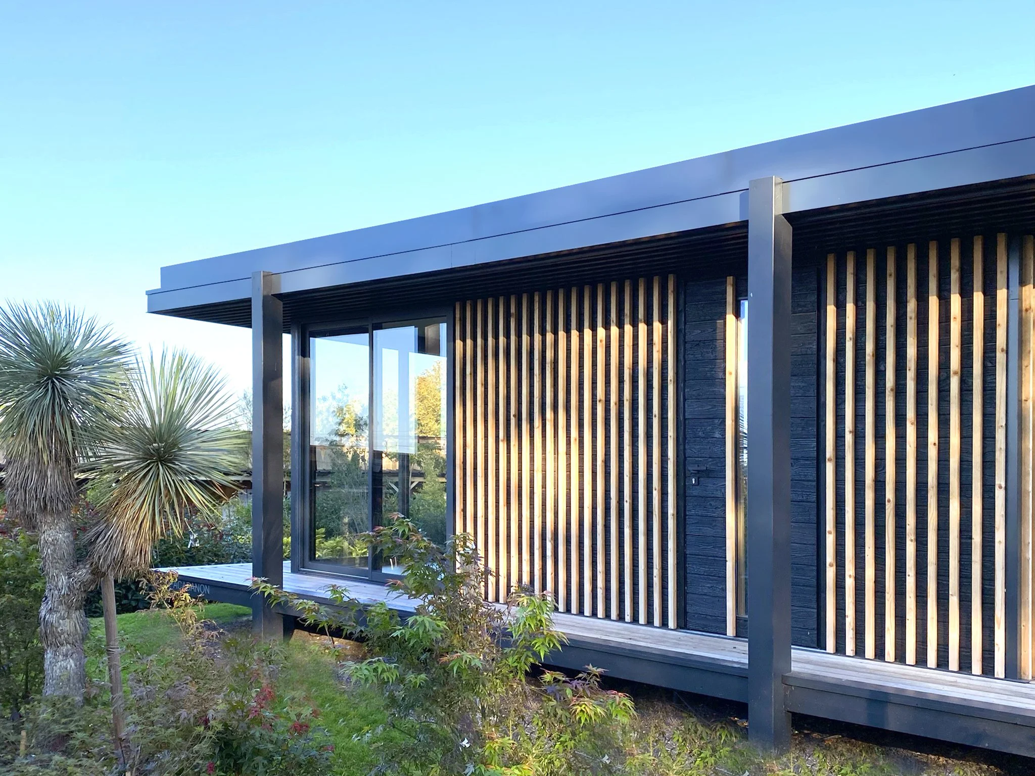 Ecolodge MEGYMA avec façade en bois et grandes fenêtres, entourée de végétation.