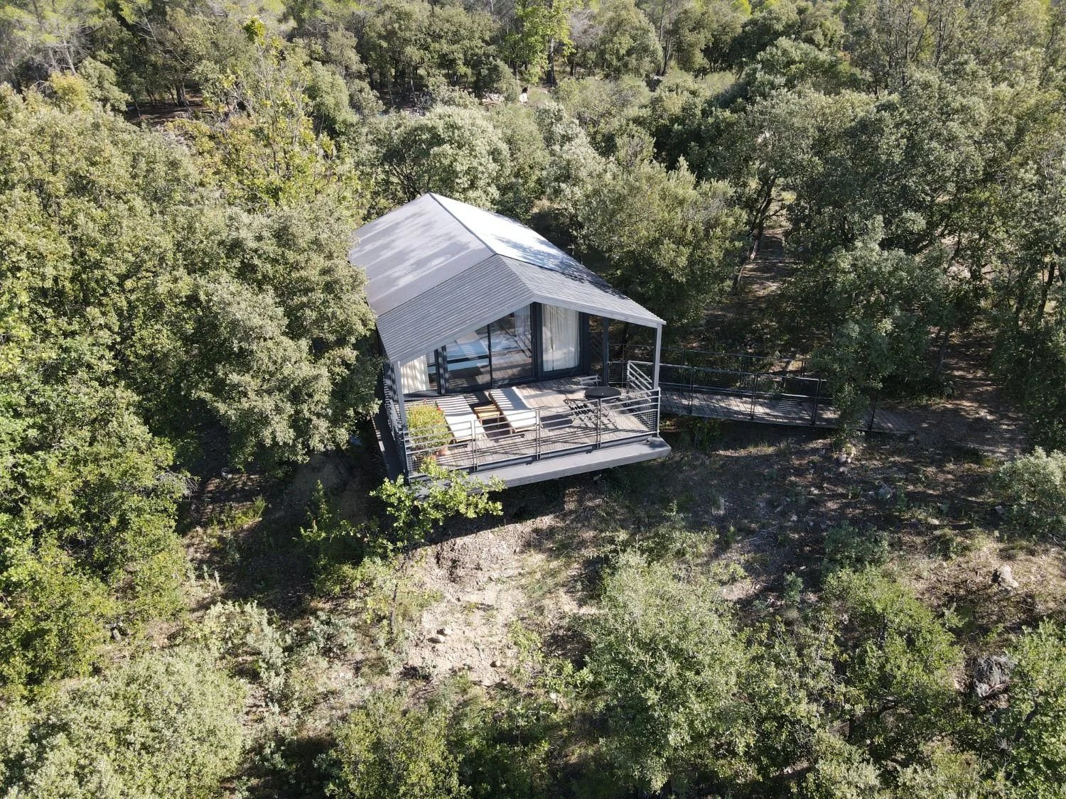 Cabane en bois moderne avec terrasse, entourée d'arbres dans une forêt.