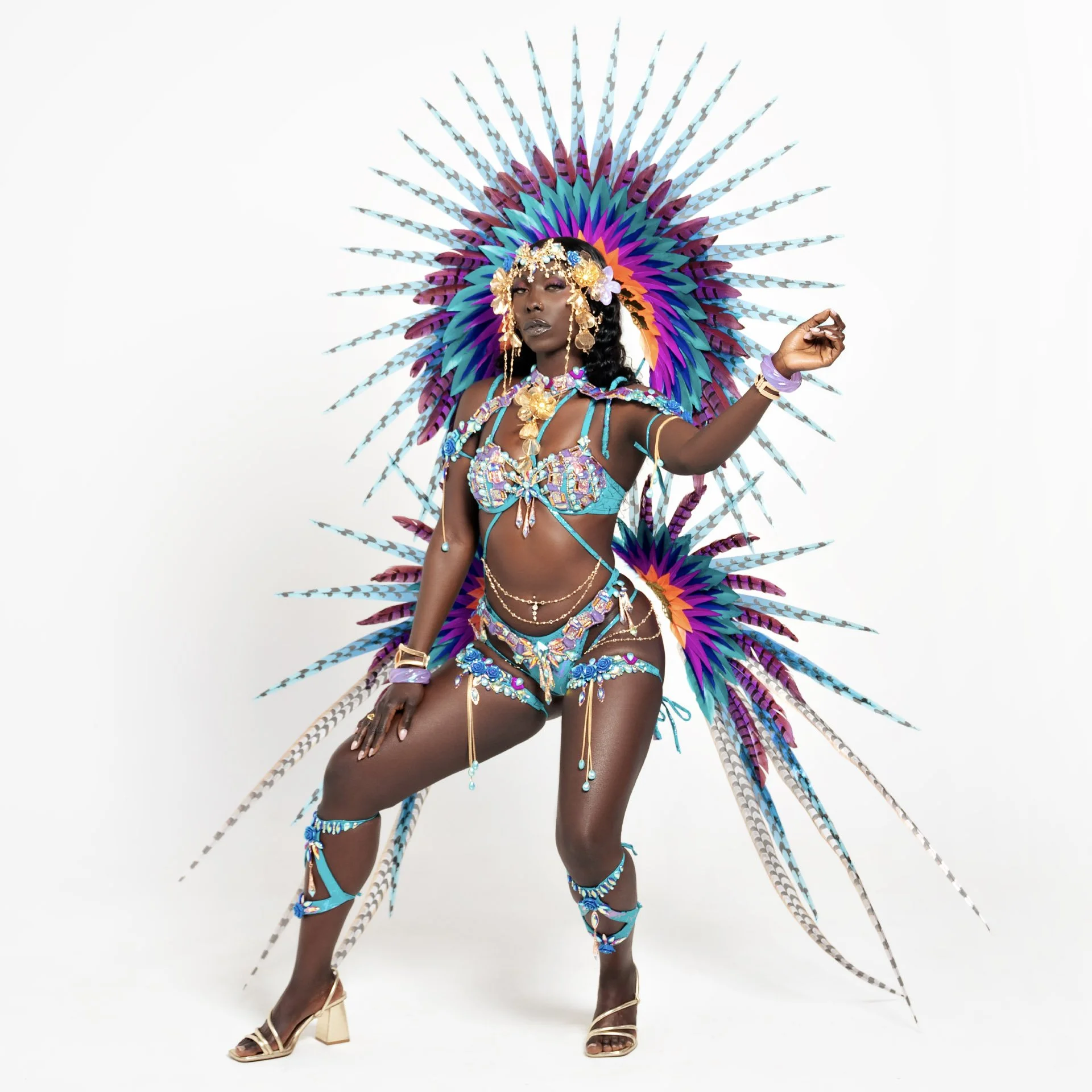 A woman in a colorful, elaborate costume with feathers, beads, and jewelry posing against a plain white background.