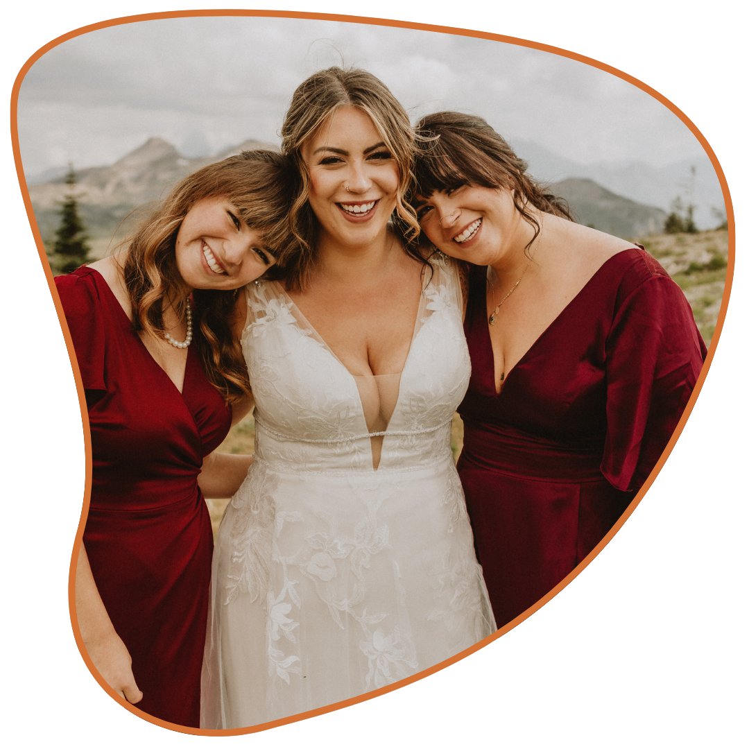 Bride with her two bridesmaids smiling on top of a mountain in Banff, Alberta during a wedding, using a gondola ride from Sunshine Village, photographed by Calgary & Alberta wedding photographer Shannon Boyd