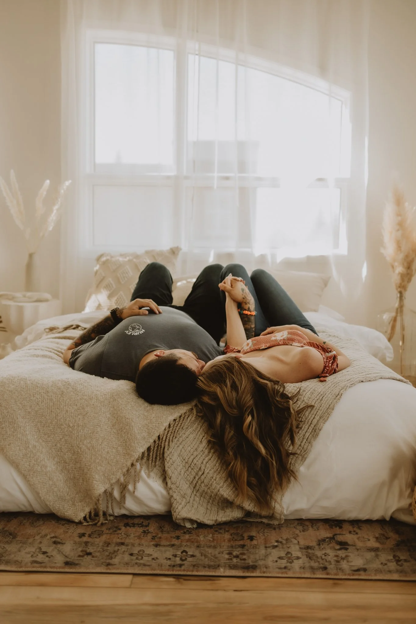 Couple lying on a bed holding hands and looking at one another during a couples session at StudioTwentyThree in St. Albert, Alberta, photographed by Calgary & Alberta lifestyle photographer Shannon Boyd