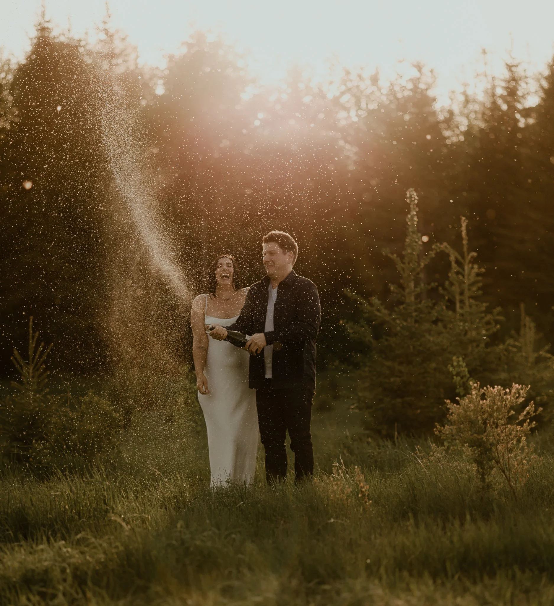 Engaged couple popping champagne during their engagement session at Riverlot 56 in St. Albert, Alberta, photographed by Calgary & Alberta engagement photographer Shannon Boyd.