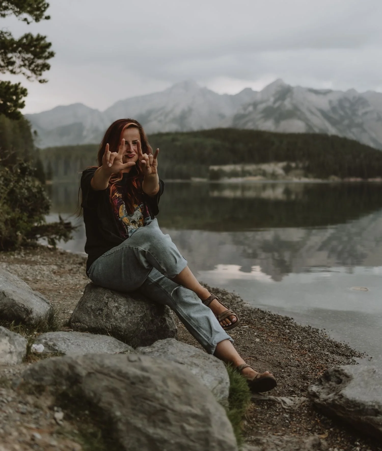 Photographer Shannon Boyd sitting on a rock at Lake Minnewanka in Banff, Alberta, captured during a self-portrait session