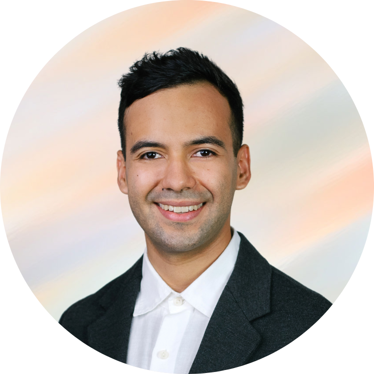 Porträt eines jungen Mannes in formeller Kleidung mit dunklem Jackett und weißem Hemd vor einem pastellfarbenen Hintergrund.