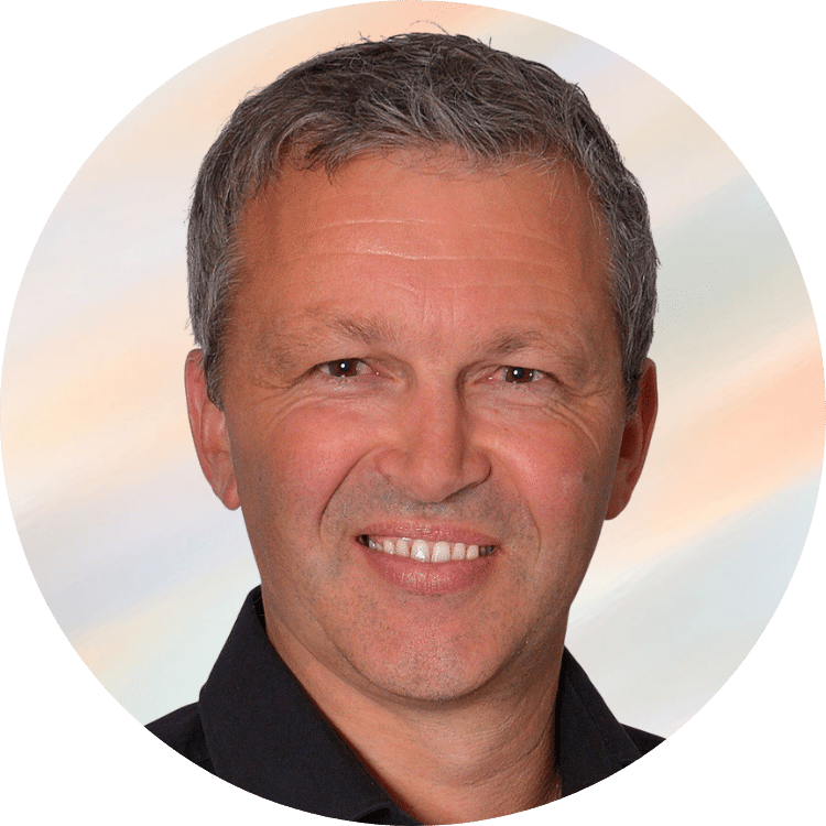 Ein Mann lächelt für ein Porträtfoto vor einem unscharfen, hellen Hintergrund.