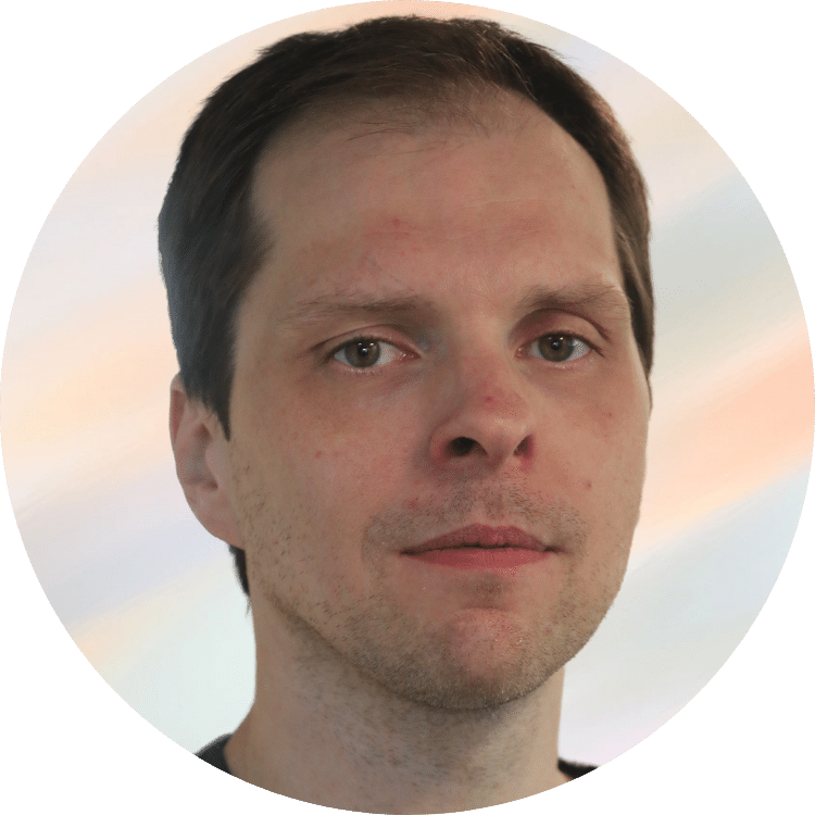 Nahaufnahme eines Mannes mit braunem Haar und leichter Gesichtsbehaarung vor einem hellen, pastelfarbenen Himmel.