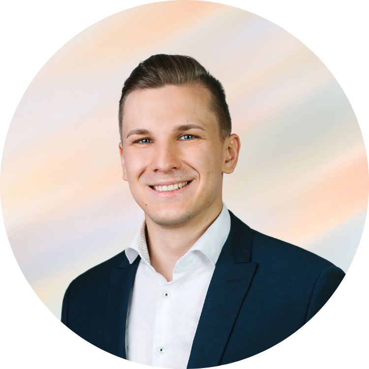 Ein junger Mann trägt einen dunklen Anzug und ein weißes Hemd, lächelt und blickt in die Kamera.