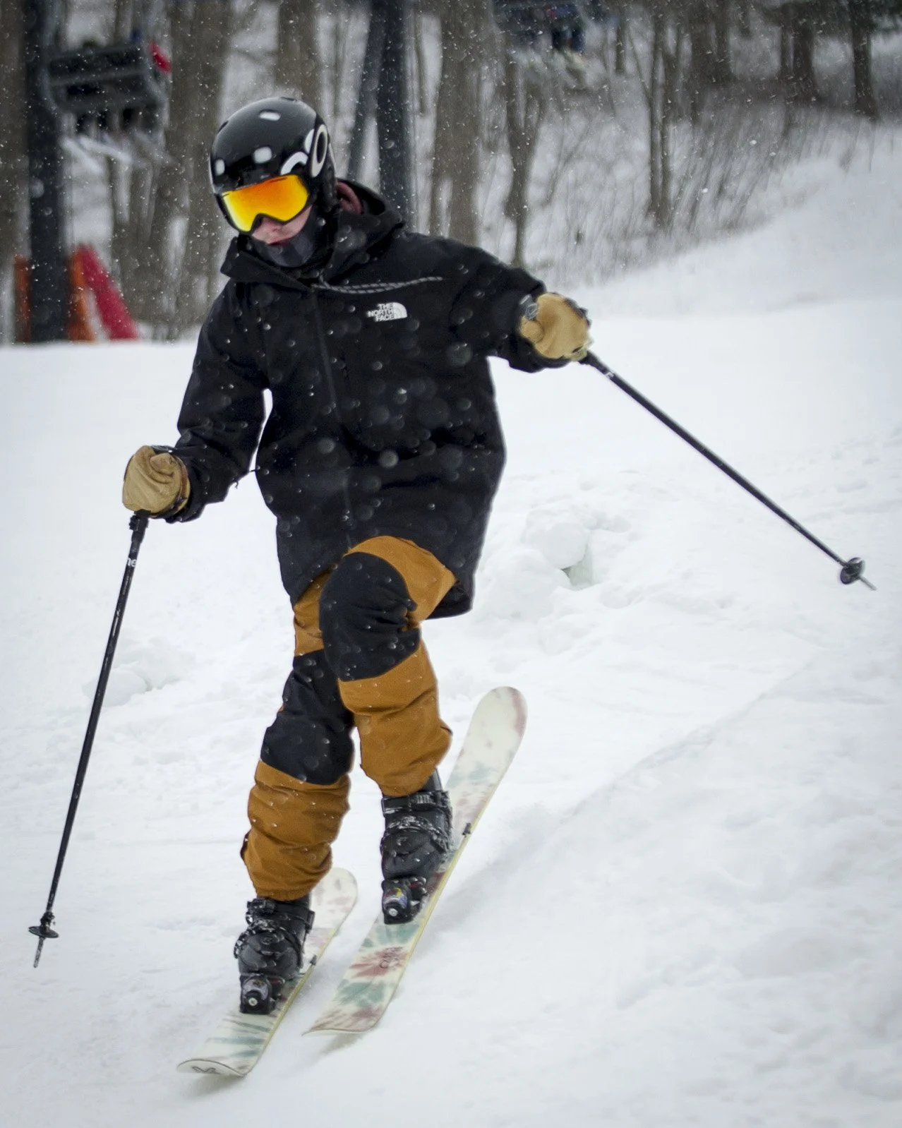 A person wearing a black jacket, yellow ski pants, a helmet, and goggles skiing on snow.
