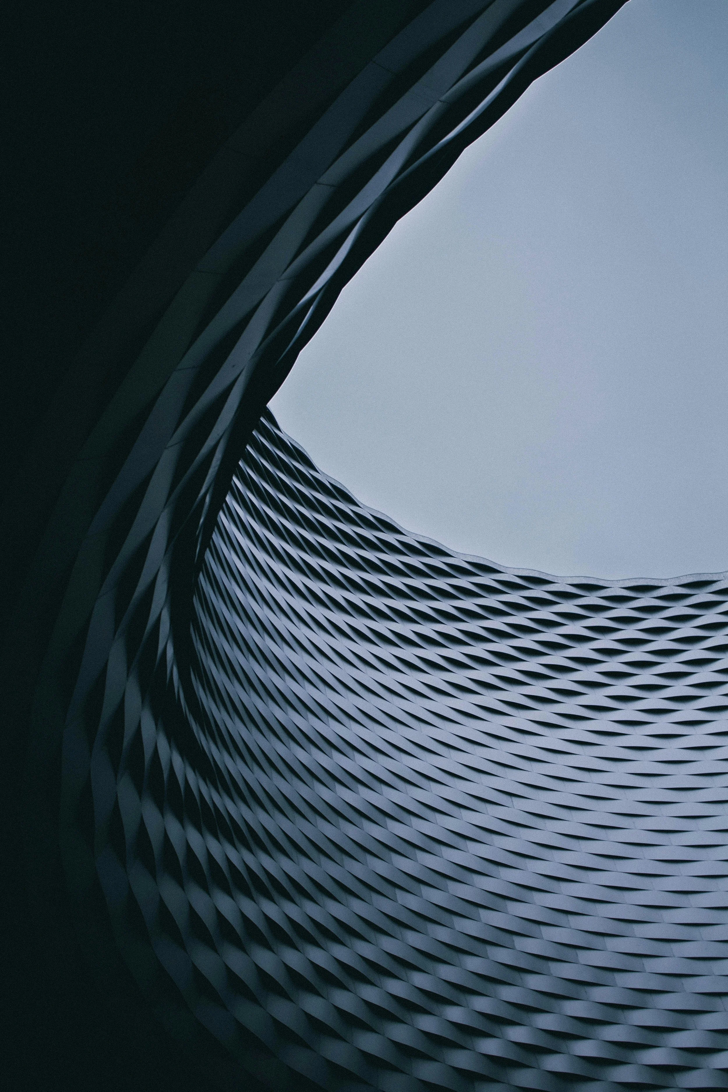 Looking up into a modern architectural building with a circular opening at the top, featuring a textured facade with repeating geometric patterns.