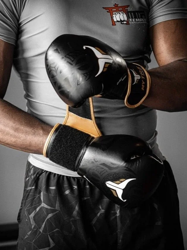 A person wearing boxing gloves and athletic shorts prepares to box in a gym.