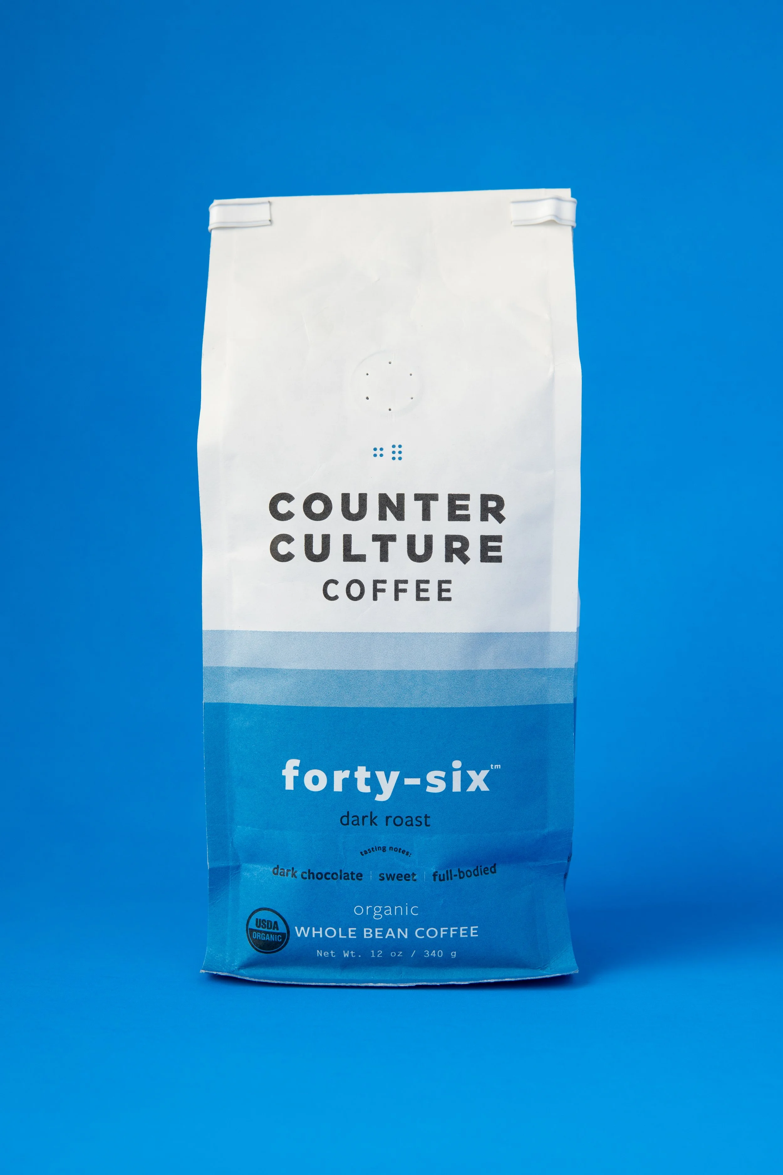 A bag of Counter Culture coffee, dark roast, 340 grams, labeled as organic whole bean coffee, with branding for forty-six, set against a blue background.