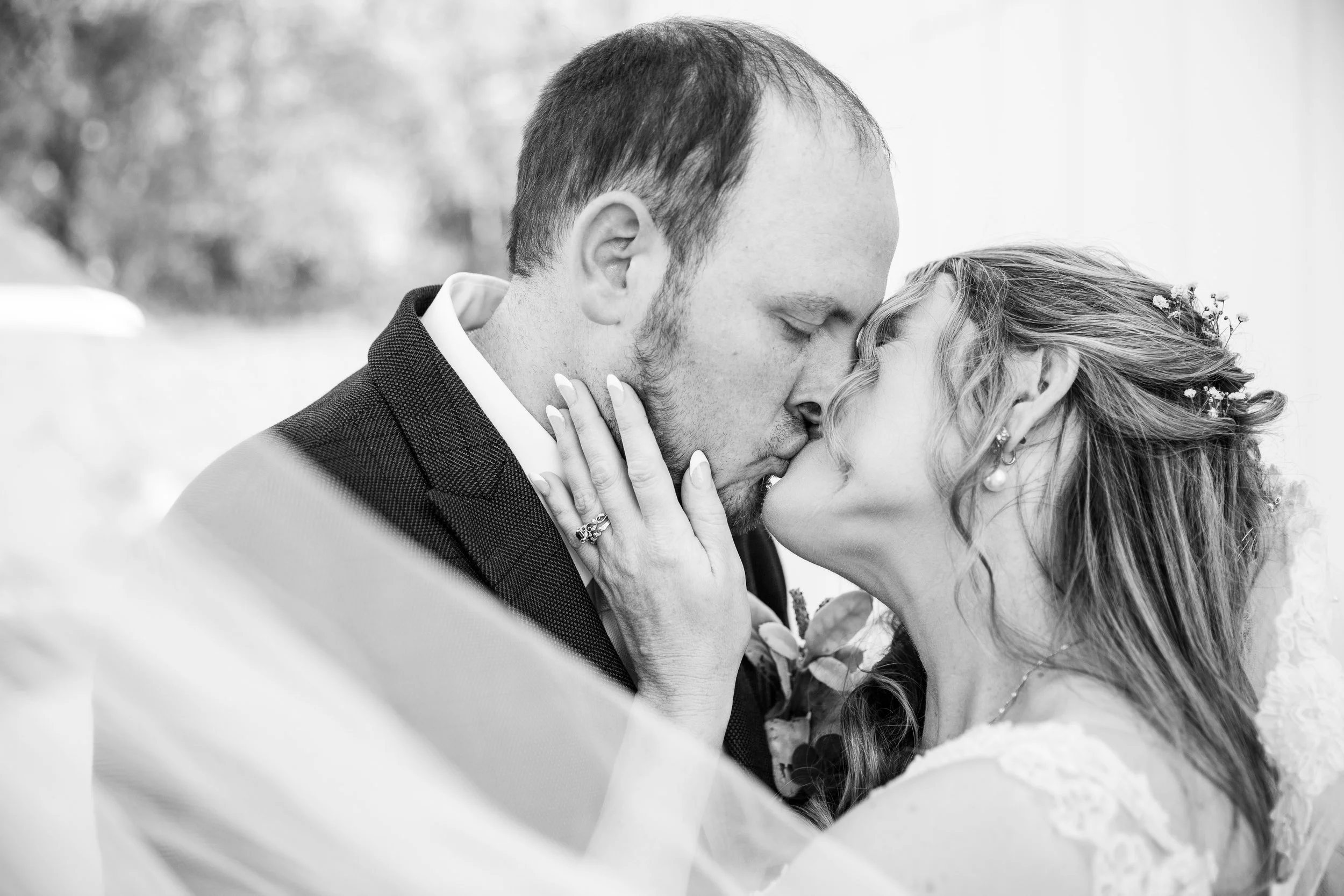 A black and white photo of a bride and groom sharing a kiss, with the bride's hand on the groom's face showing her wedding ring.