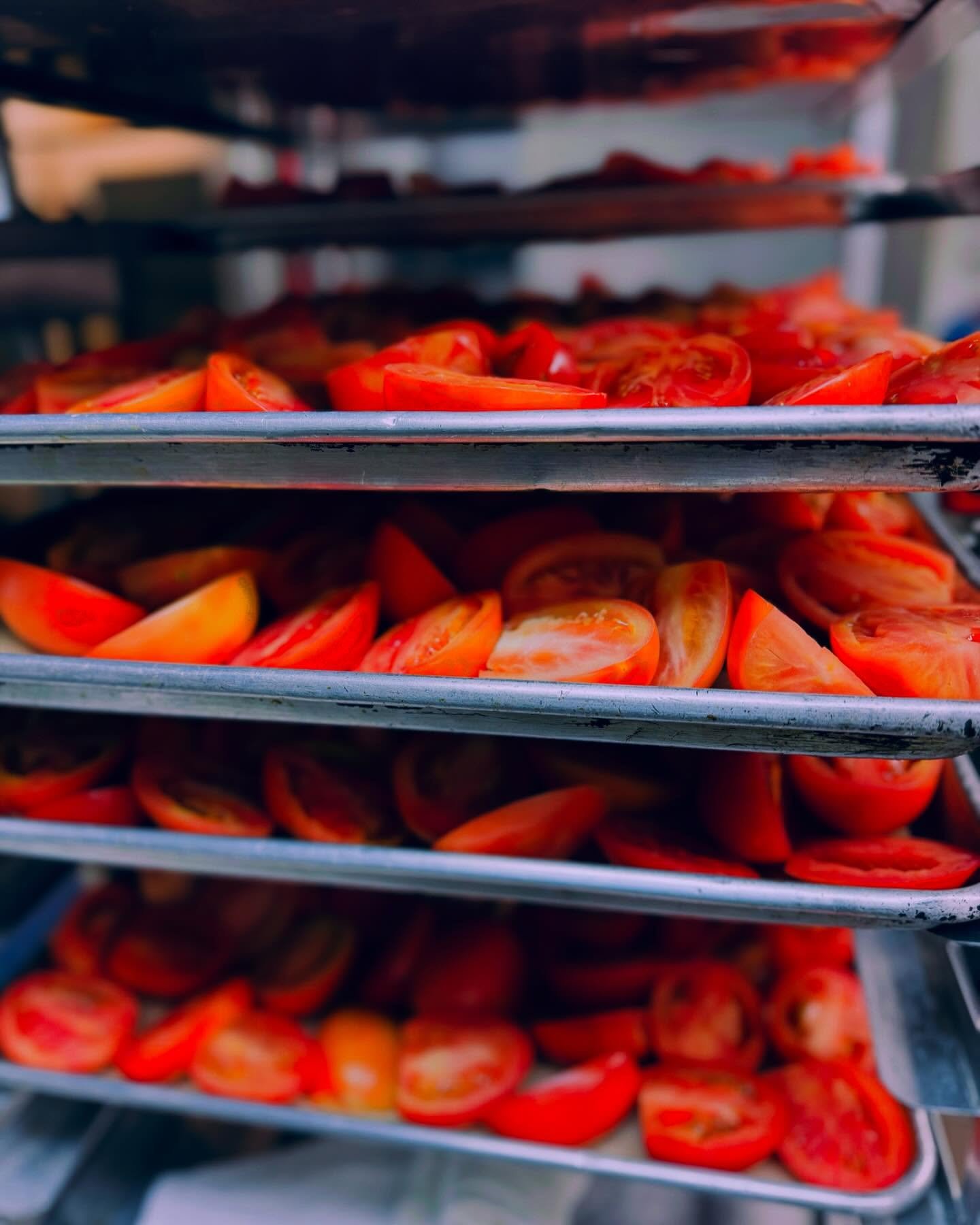 Sliced tomatoes on metal trays in a commercial kitchen or food prep area.