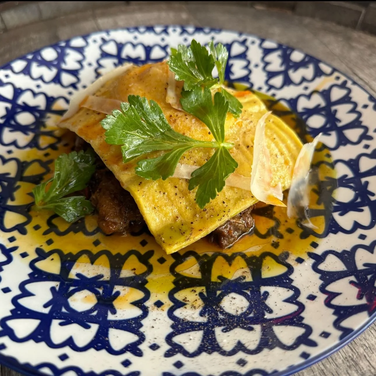 A plated Mexican dish with beef, covered by a folded yellow egg omelet, garnished with cilantro leaves and onion slices, served on a blue and white patterned plate.