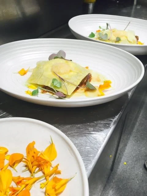 Plate with stuffed pasta, garnished with edible flowers and microgreens, in a professional kitchen.