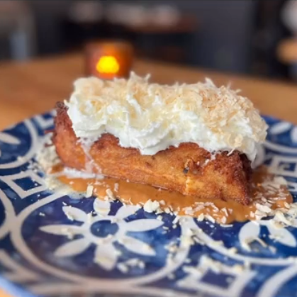 Slice of dessert with whipped cream and toasted coconut on a blue and white patterned plate