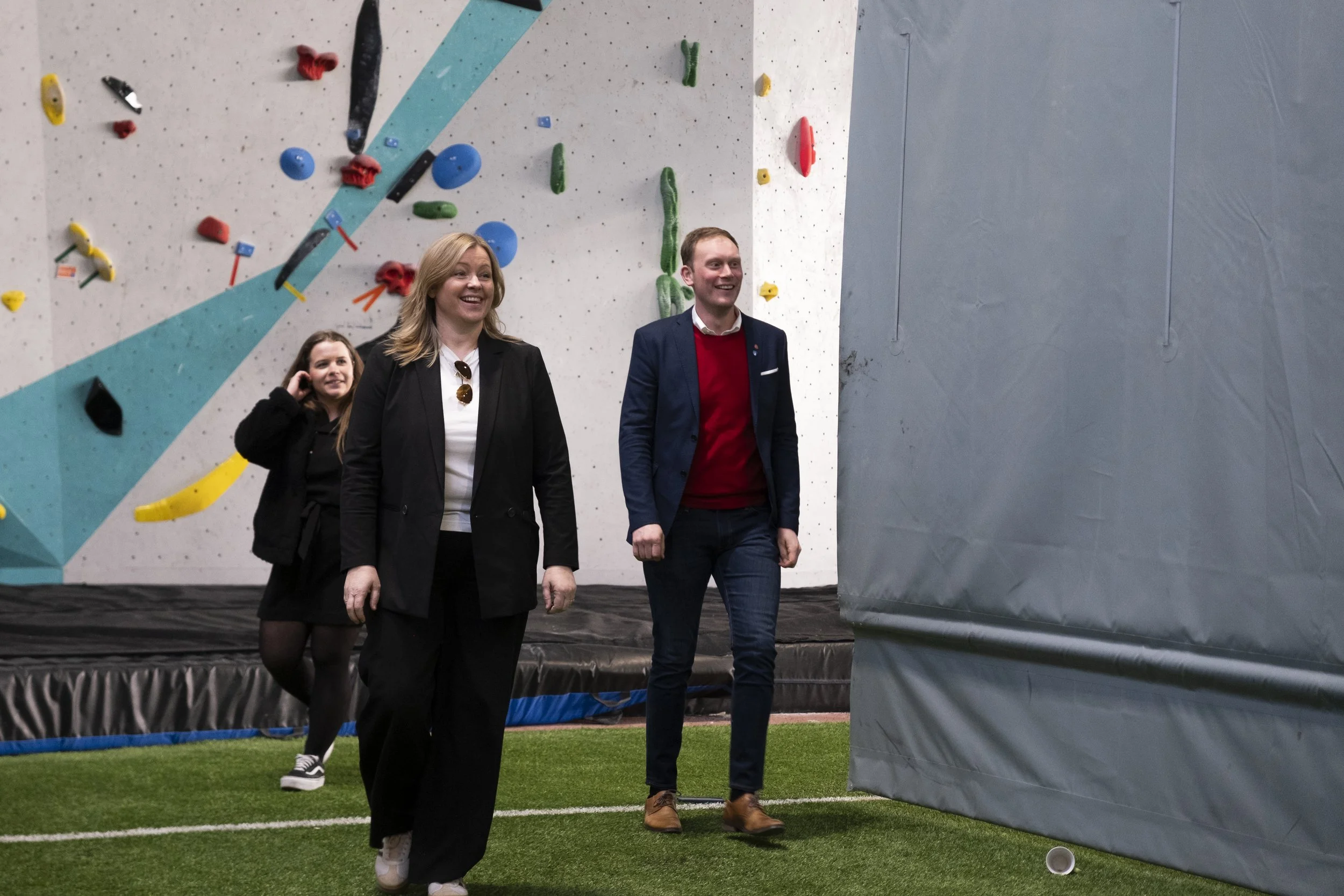 Tre mennesker går inn i en innendørs klatreveggesal. Det er Kommunal- og distriktsminister
Kjersti Stenseng (Ap), Stig Ove Ølmheim (AP) og kommunkasjonsmedarbeider. Kvinner og en mann smiler og ser fornøyde ut. Foto: Benjamin Haug-Toklum