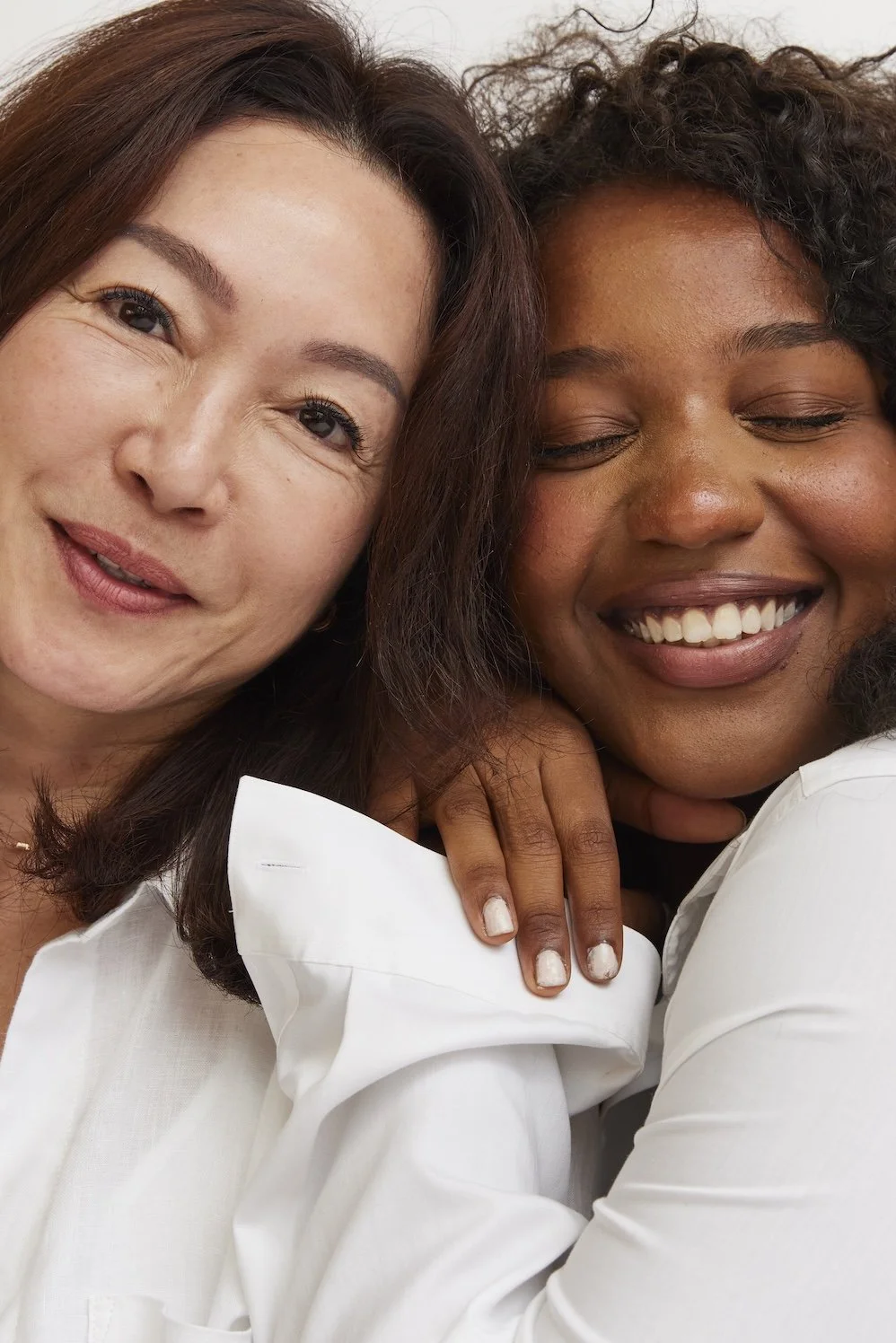 Two women close together, smiling and showing affection, with one resting her hand on the other's shoulder.