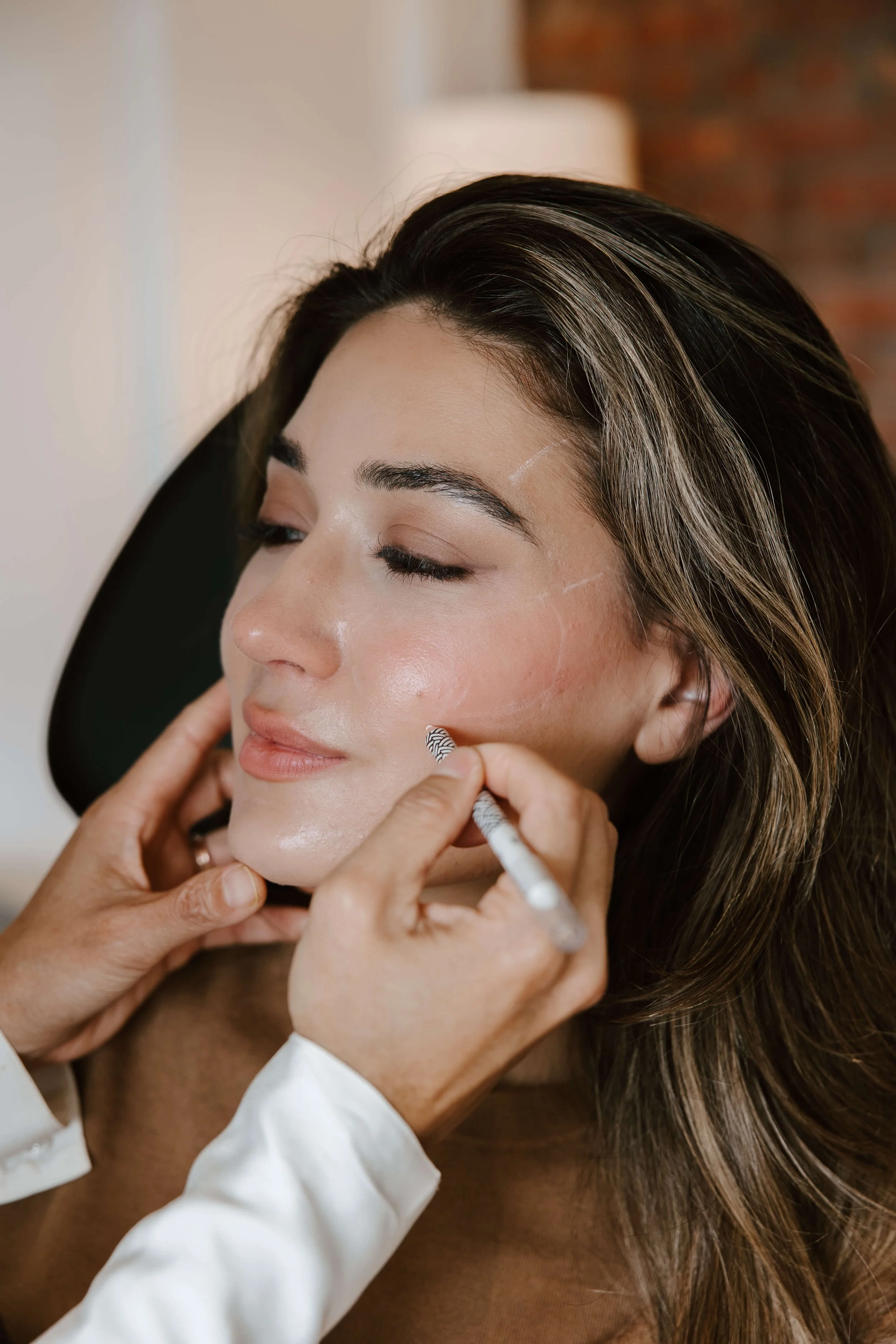 A woman receiving a facial treatment, with an aesthetic injector mapping her face prior to treatment