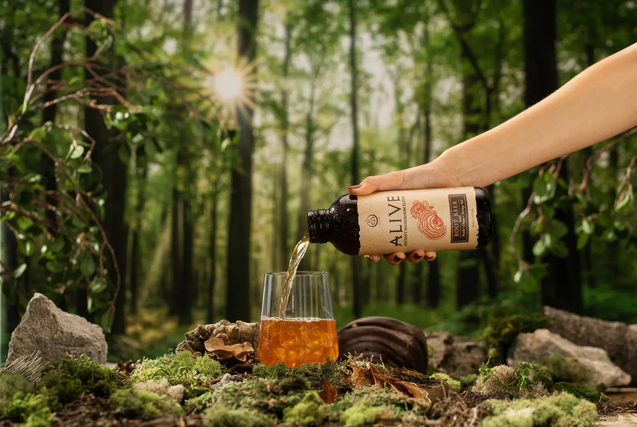 Person pouring Amber Ale from a bottle into a glass in a forest setting with rocks and moss on the ground.