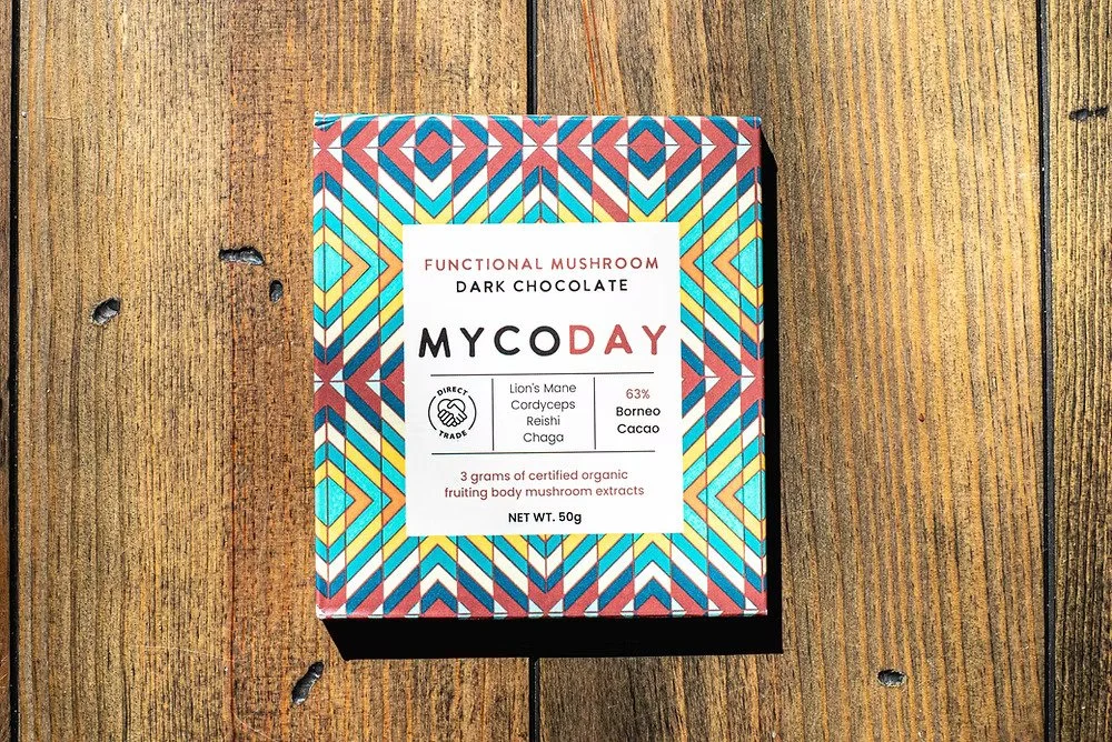 Packaging of a dark chocolate mushroom with a colorful geometric pattern on the box, placed on a wooden surface.