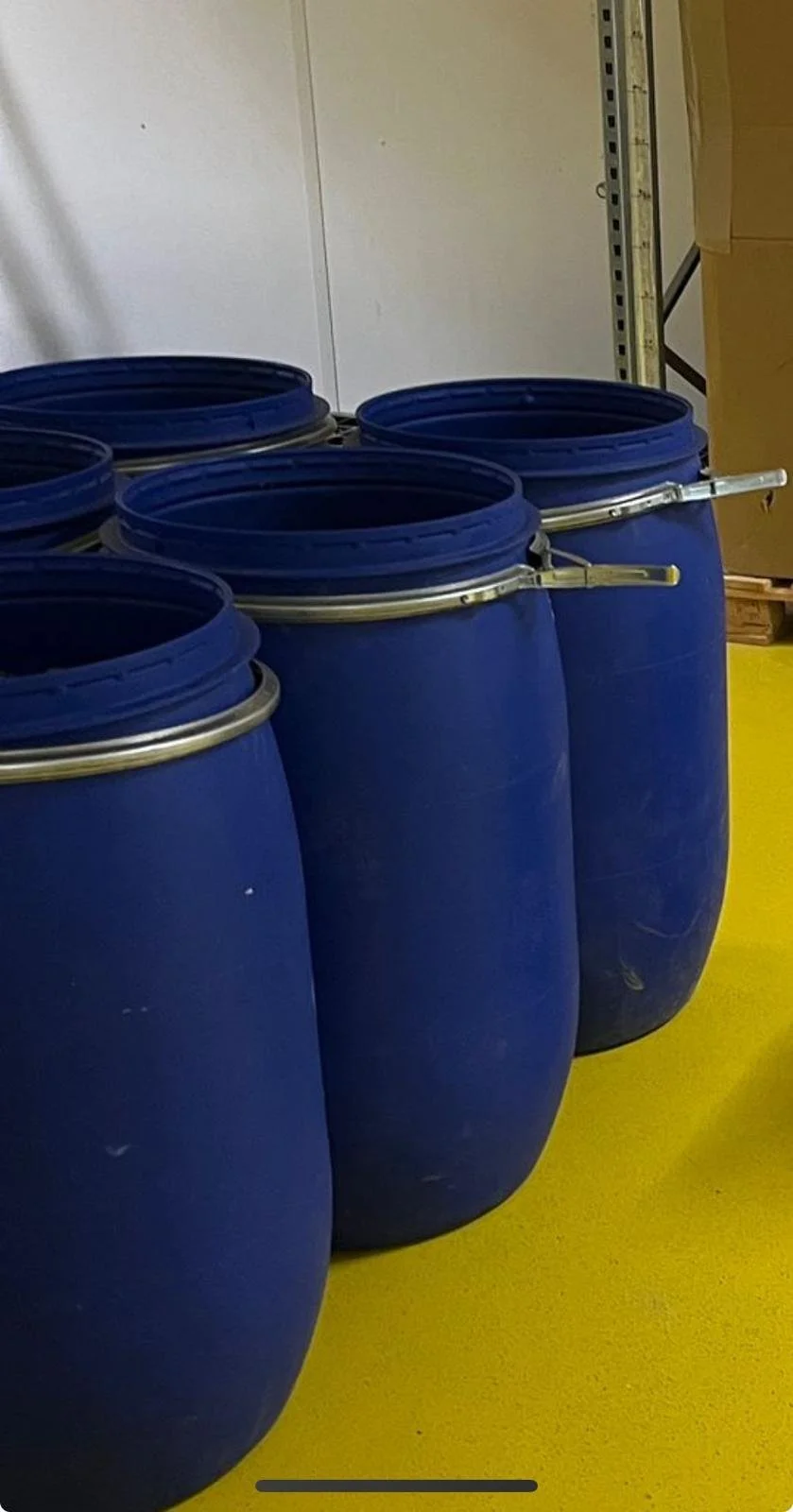 Close-up of a glass jar filled with dried cannabis buds, with other containers and a wooden stick in the background.