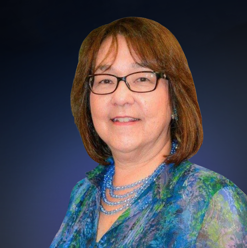 A woman with shoulder-length brown hair, glasses, and blue jewelry, wearing a multicolored patterned blouse, smiling against a white background.