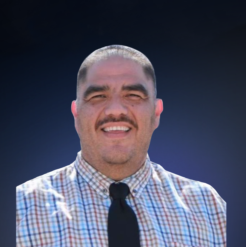 A smiling man with short dark hair, a mustache, wearing a checkered shirt and a black tie against a plain white background.