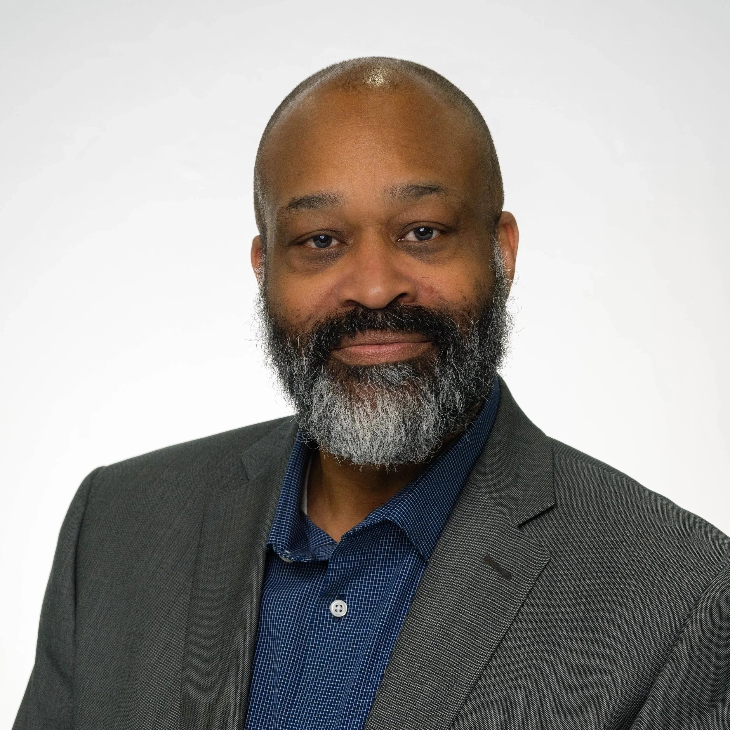 A man with short hair, glasses, and a big smile, wearing a suit, white shirt, and striped tie, outdoors with a dark, blurry background.