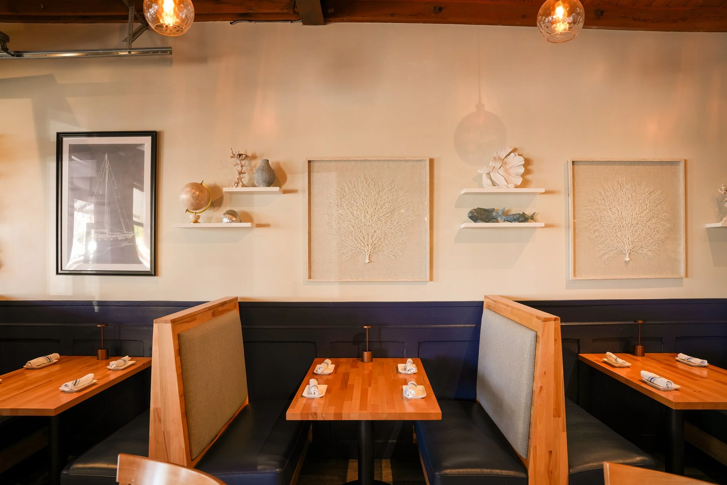 Interior of a restaurant with wooden tables, booth seating, and decorative wall art including framed cosmic and coral designs, as well as shelves with sculptures and globes.