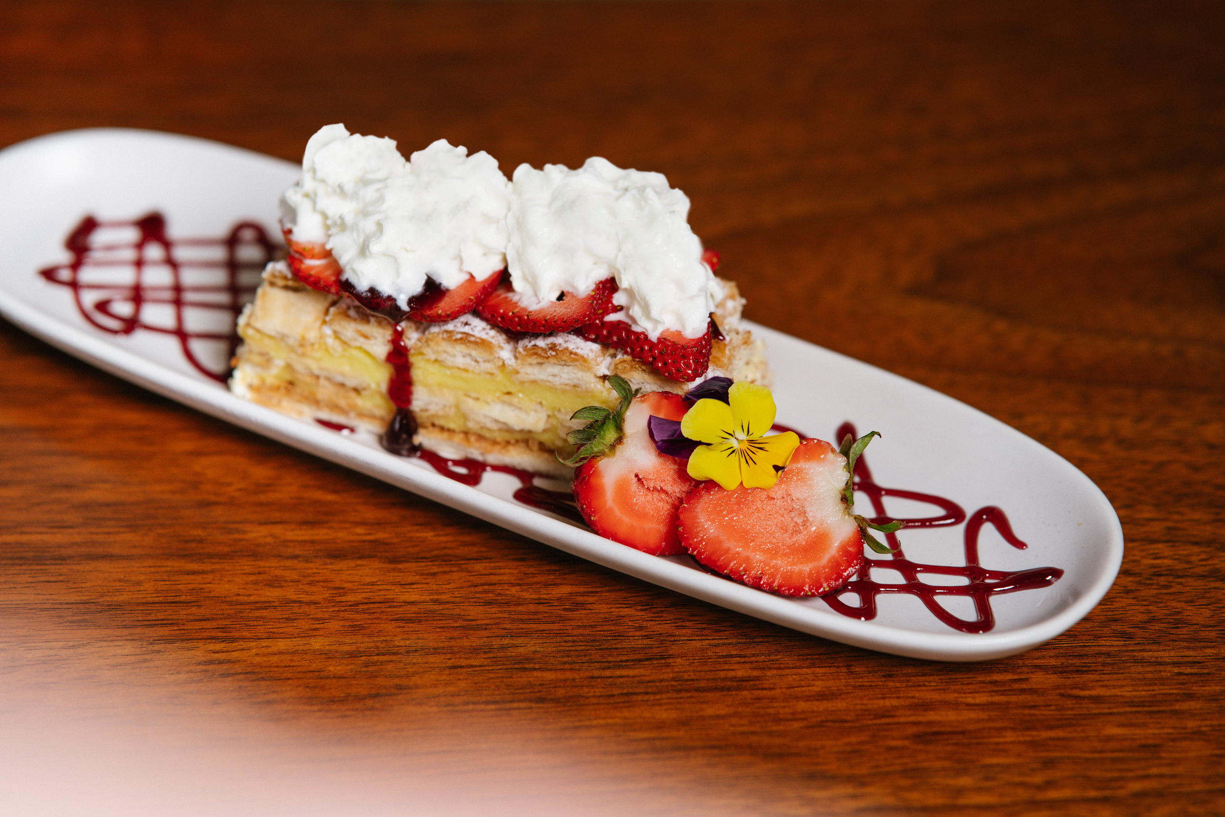 A slice of cake with strawberries on a rectangular white plate.