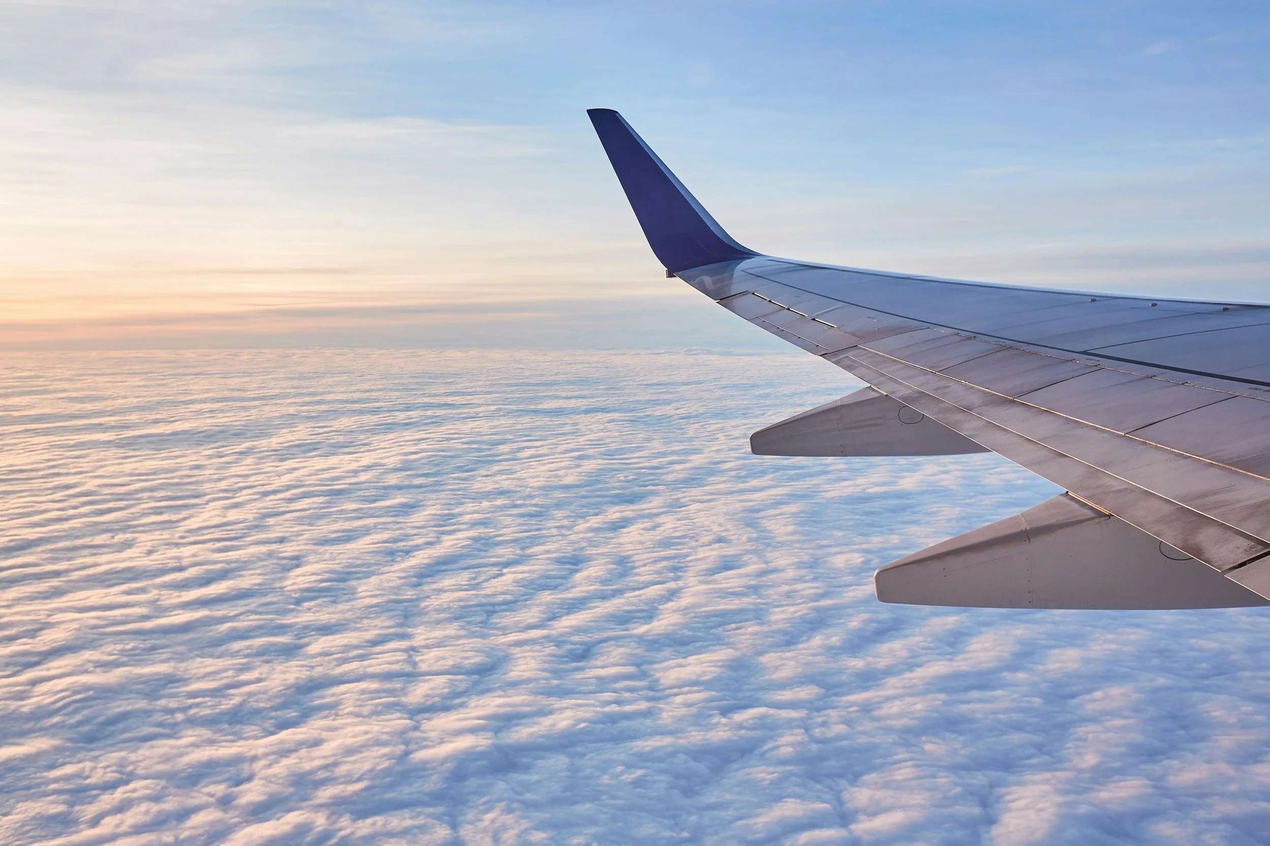 View of an airplane wing above a sea of clouds during sunset or sunrise.