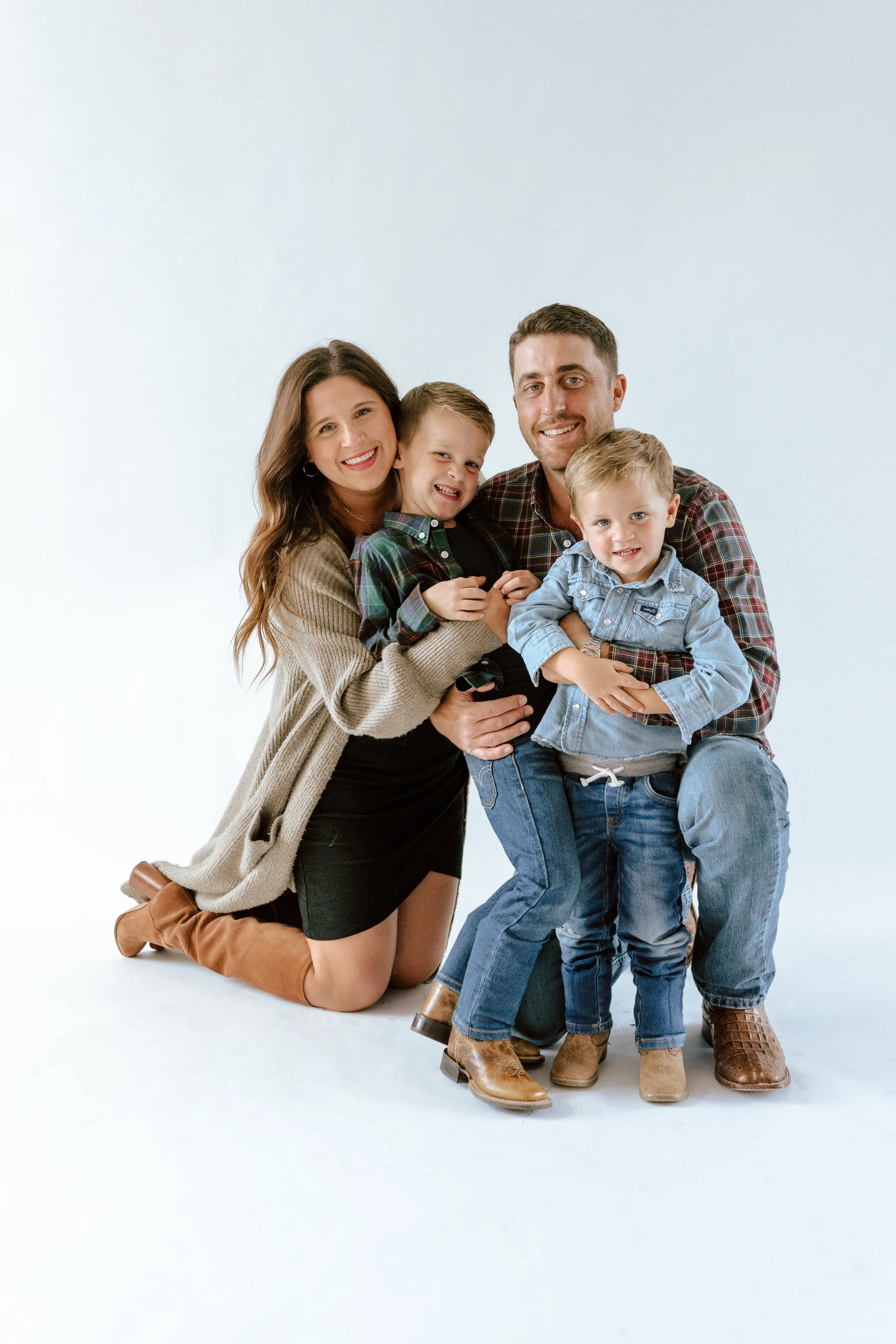 Family of four with two young boys posing together, smiling, on a white studio background.