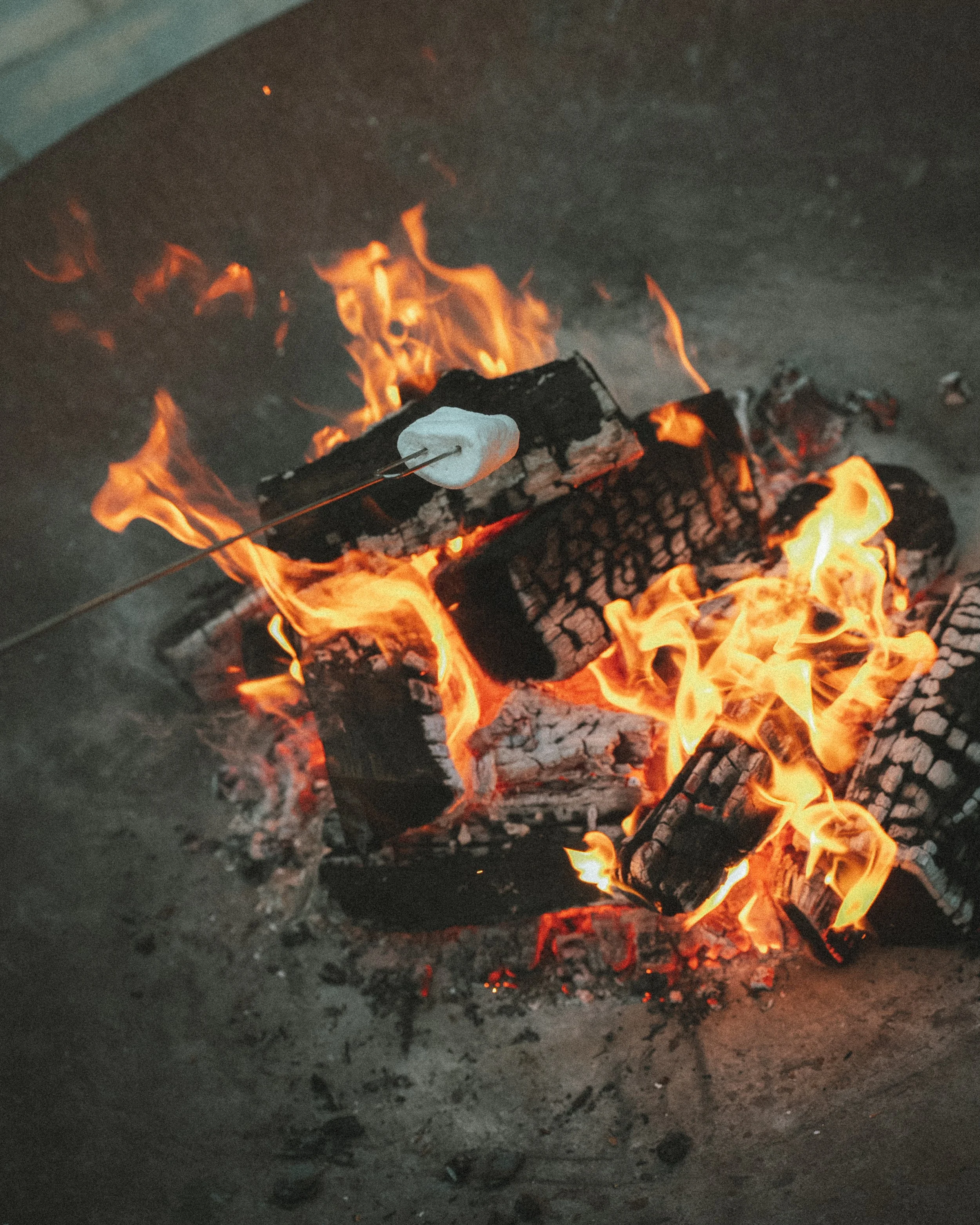 A small campfire with burning logs and bright orange flames on a dirt ground.