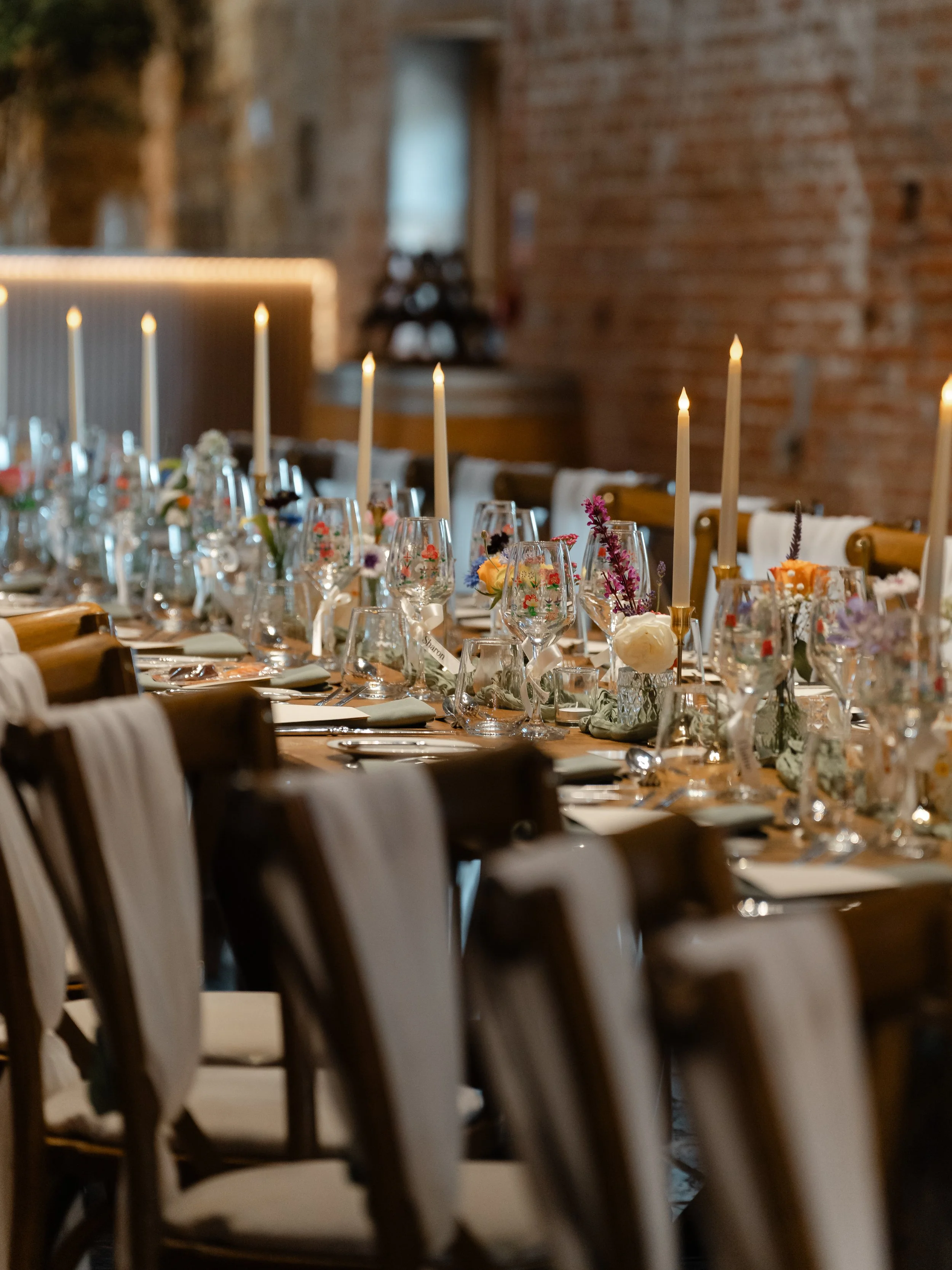 Decorated dining table with flowers and candles in a rustic brick-walled room.