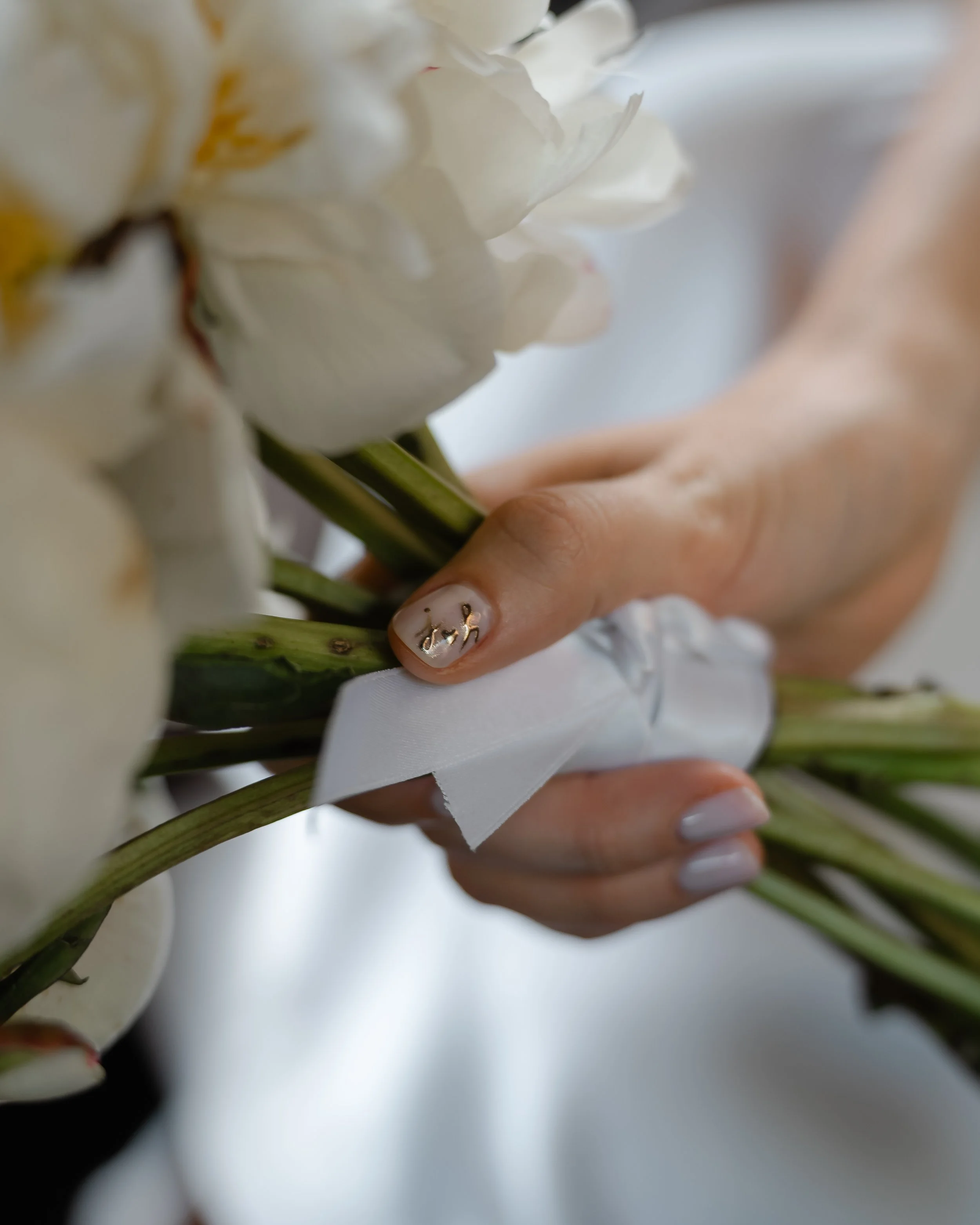 Close-up of white flowers being held by a person's hand with decorated nails. The focus is on the flowers and hand, with a blurred background.