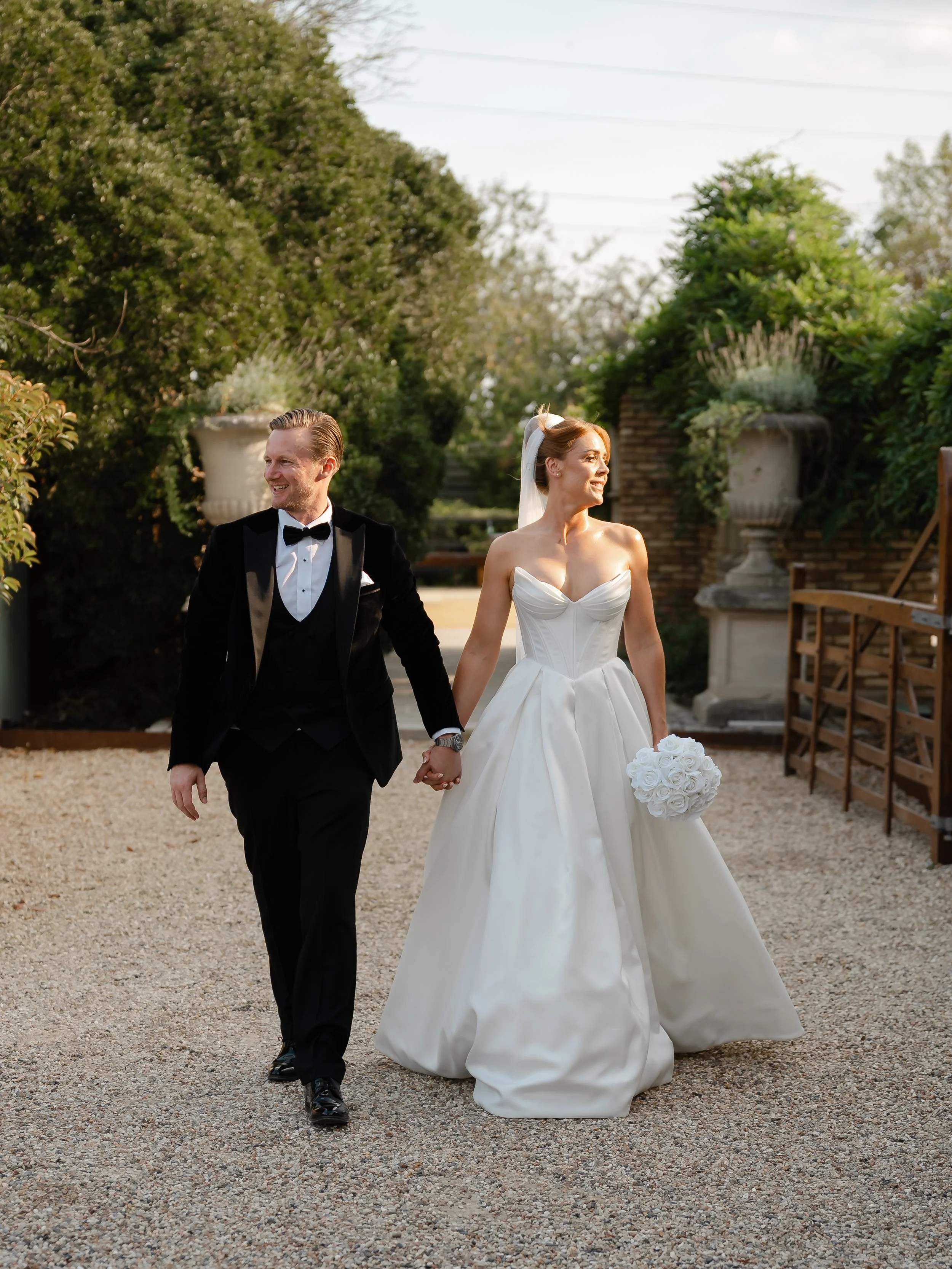 A bride and groom walking hand in hand outdoors, dressed in wedding attire, smiling and enjoying their wedding day.